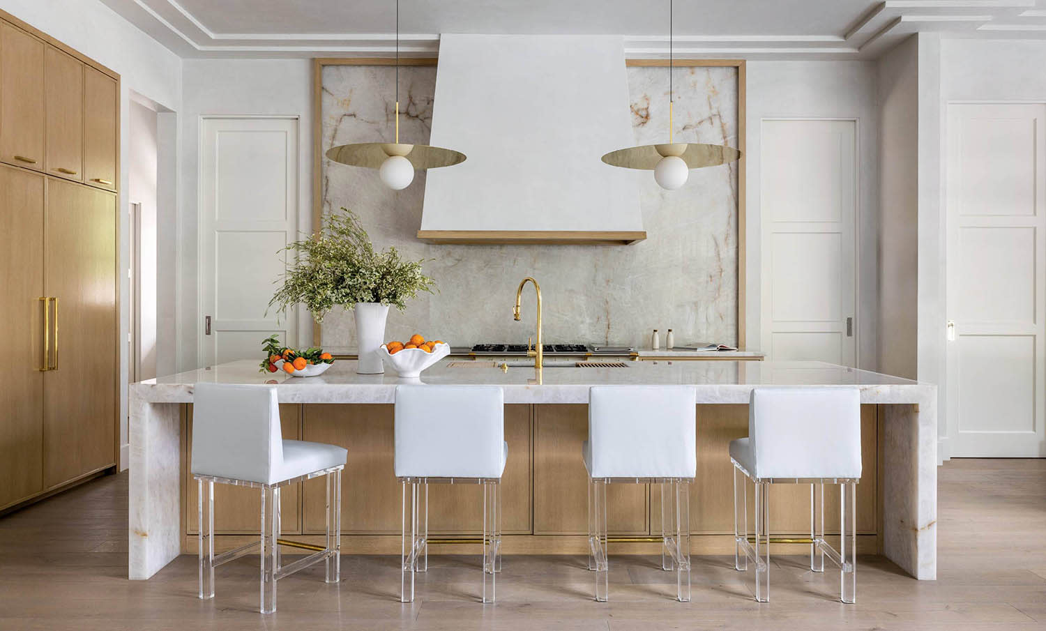 Kitchen stools with clear legs sit at an island with quartzite countertops and matching backsplash.