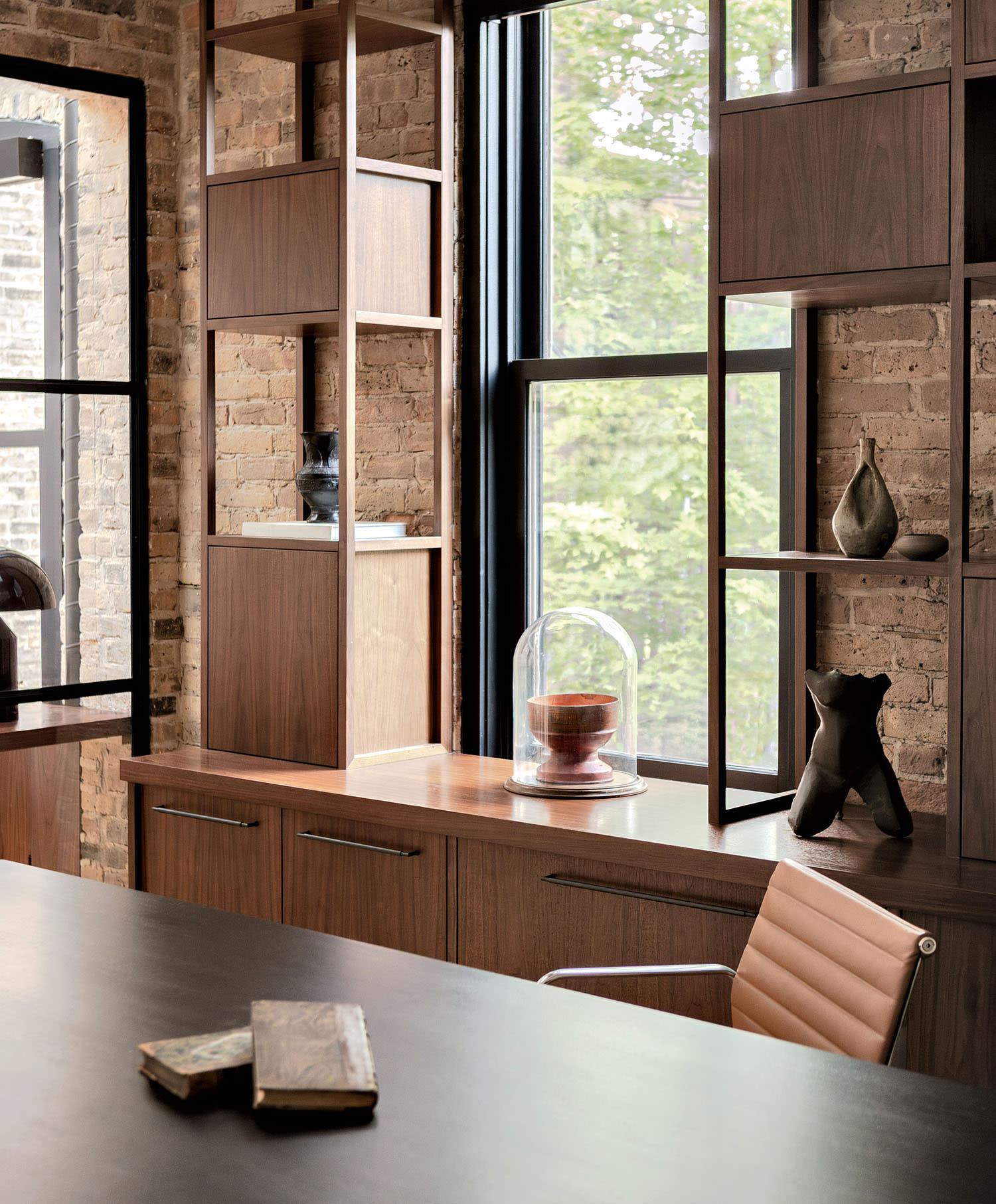 A desk sits in front of wood filing cabinets and matching shelving with decorative items near a window.