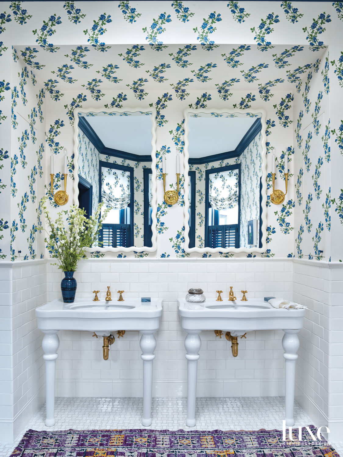 A bathroom with blue-and-white floral wallpaper. Two white pedestal sinks stand next to each other.