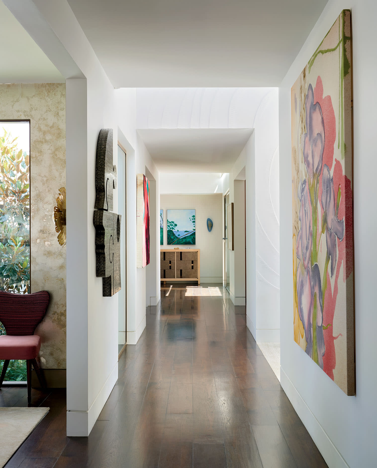 Modern hallway with wooden floors and white walls, adorned with vibrant abstract paintings on both sides. Sunlight filters through the space, creating a serene ambiance.