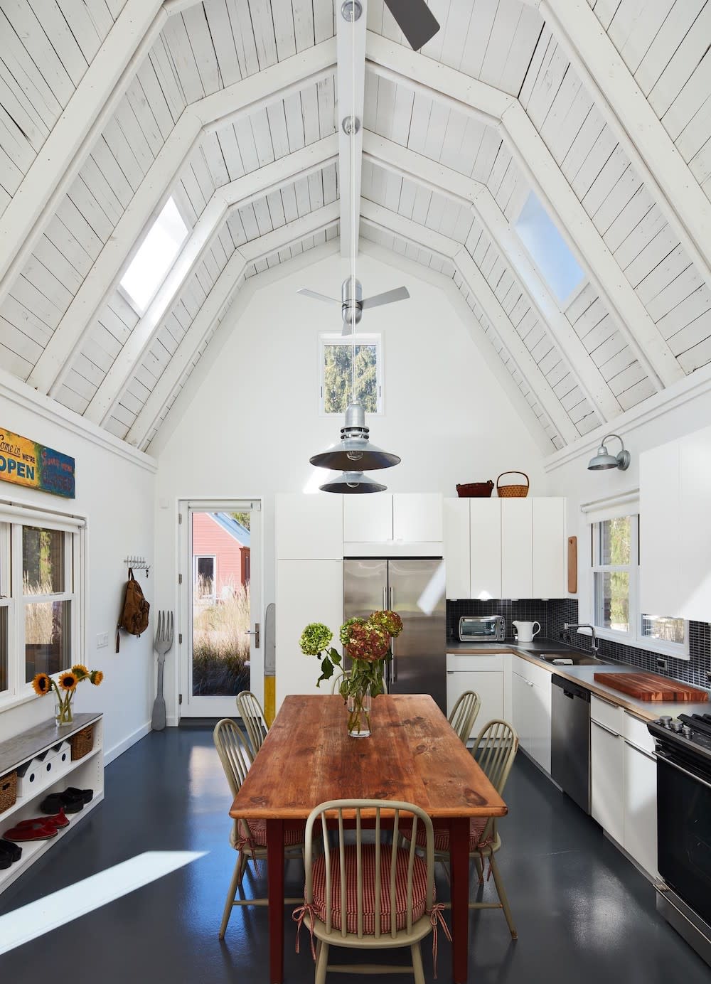 Barn converted into large open kitchen space. High ceilings with white beams, stainless pendants hang above the rustic wooden table.