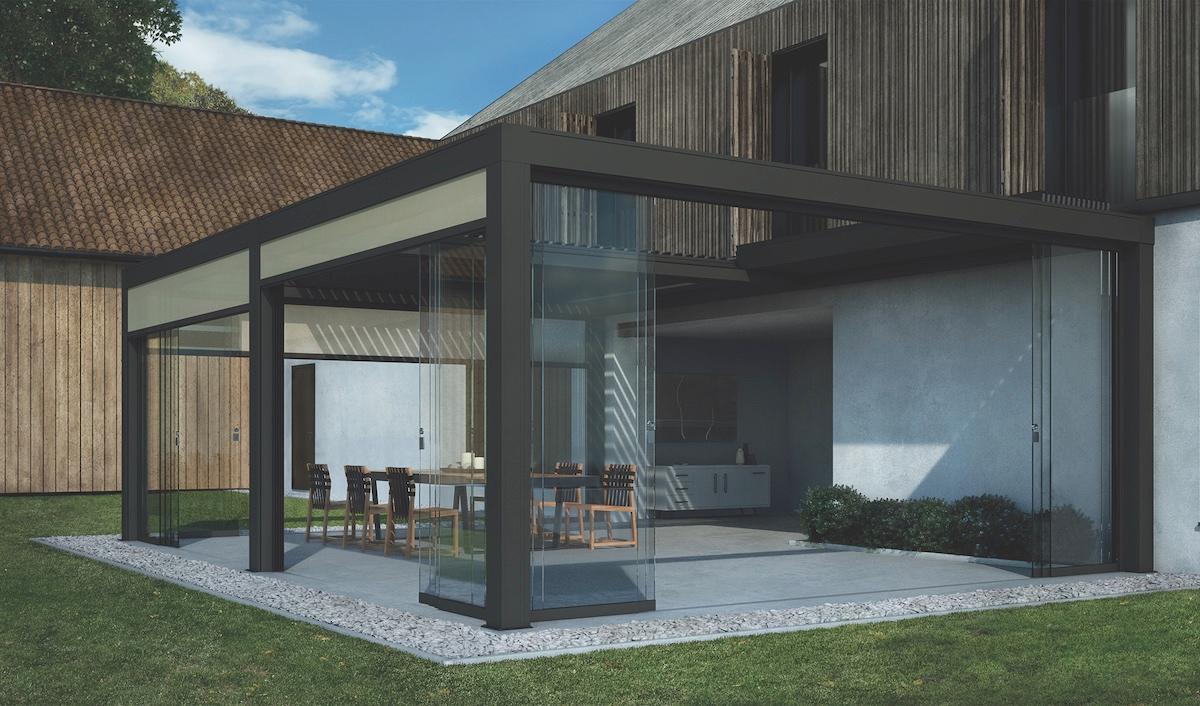 Minimalist glass pergola attached to a modern home, enclosing an outdoor dining area with sliding glass panels and clean-lined architecture.