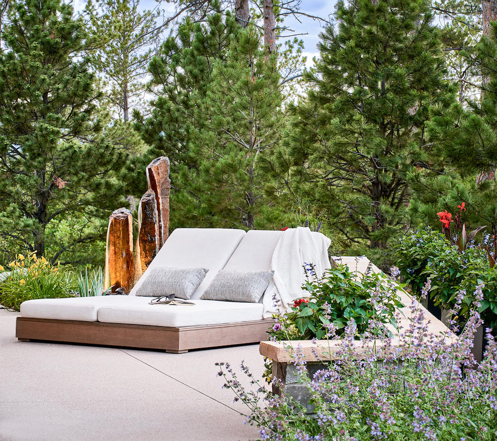 A white lounge chair on a concrete patio, adorned with colorful flowers, offers a serene spot to relax.