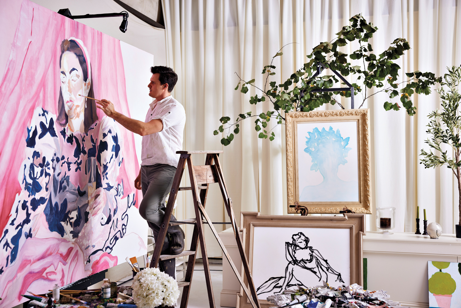 Daniel Zimmerman stands on a ladder while painting within a fabric-surrounded room