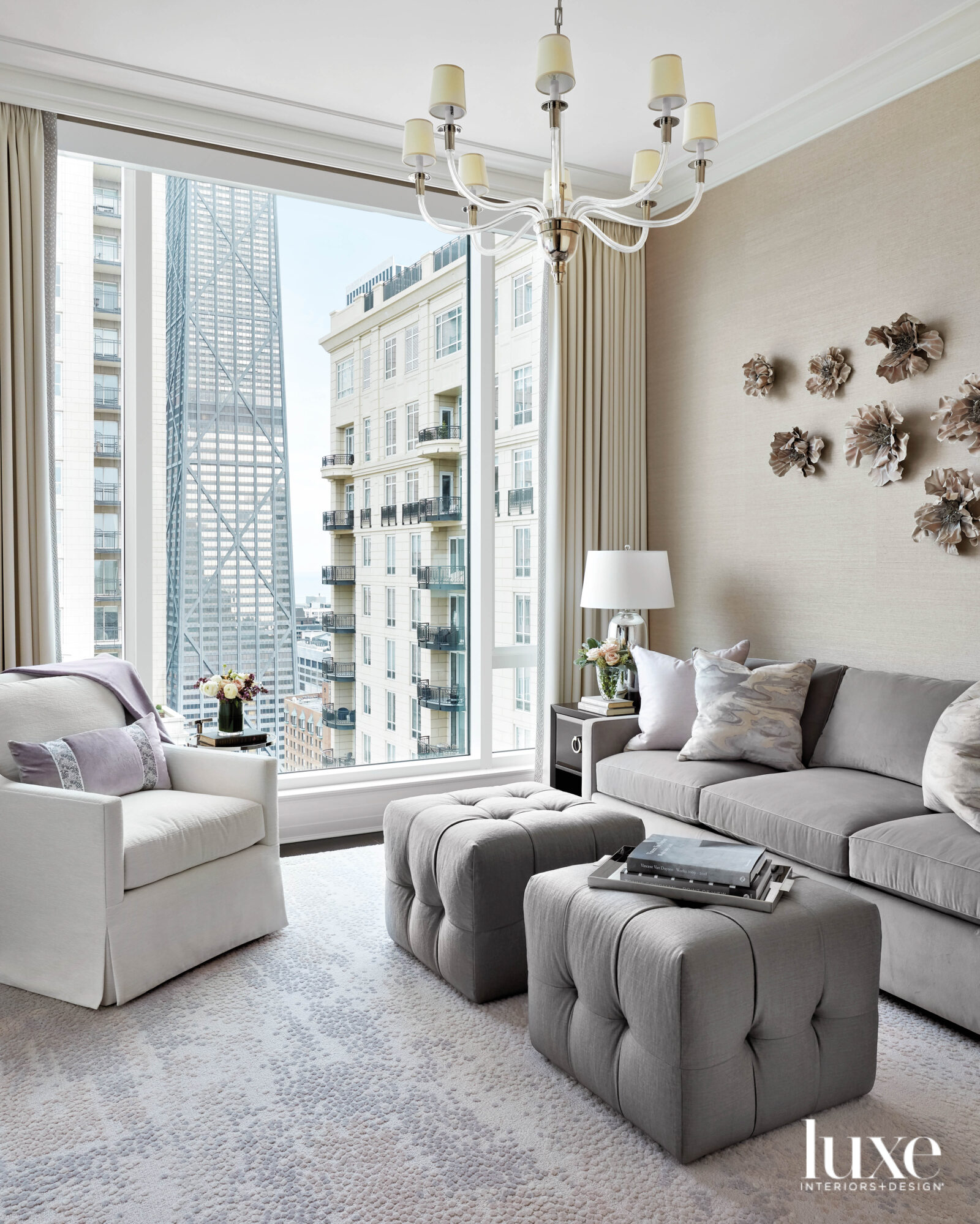 A seating area with a gray couch, two gray ottomans and a white chair. Behind the couch hangs sculptures of a flowers.