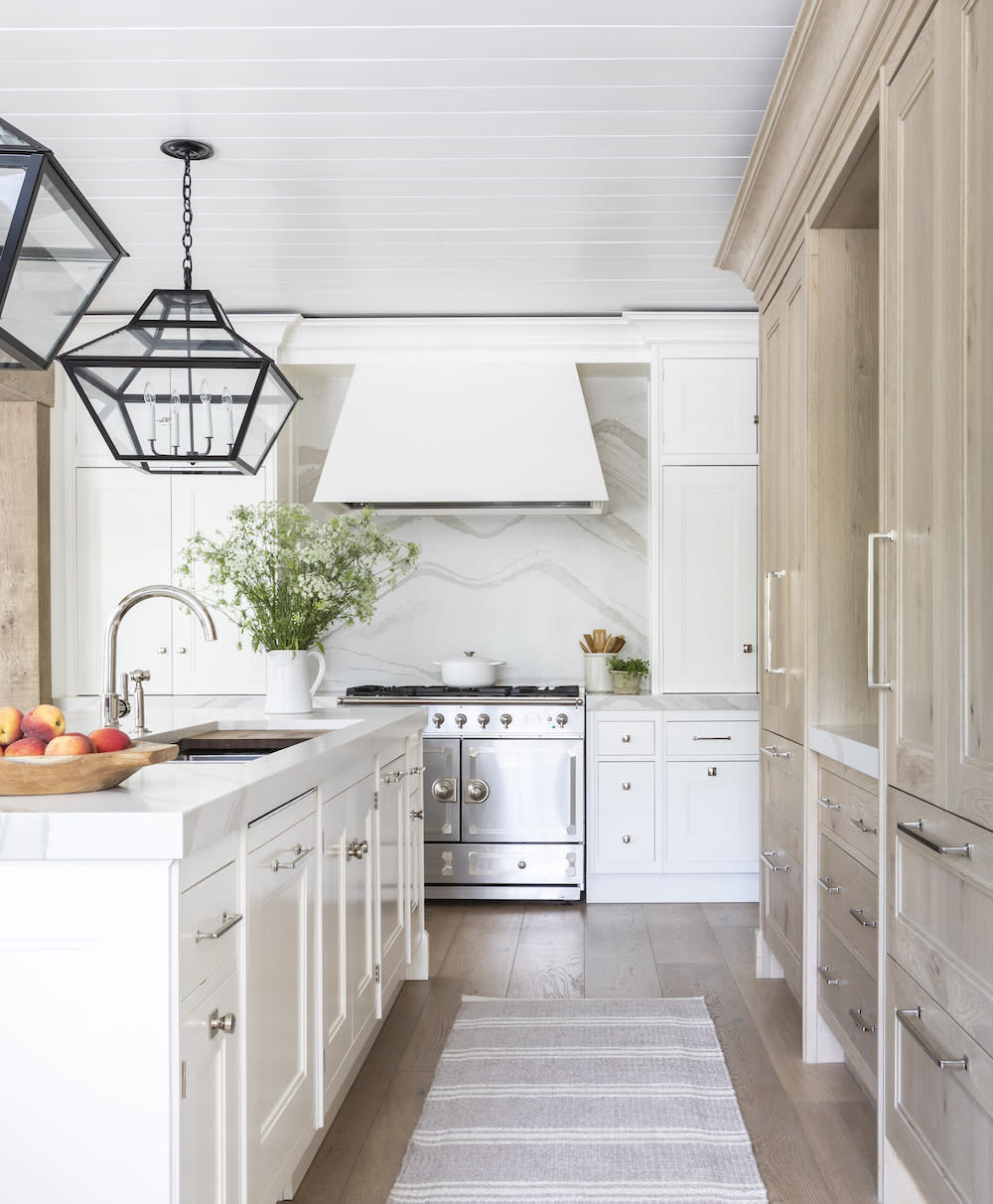 A mix of white and natural cabinets in this white kitchen with marble backsplash behind white oven hood and statement lighting.