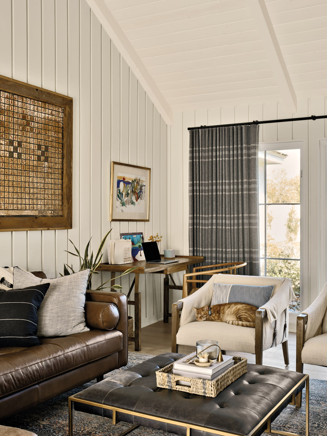 Sitting room with brown leather sofa, gray plaid curtains, white chairs and a black leather ottoman