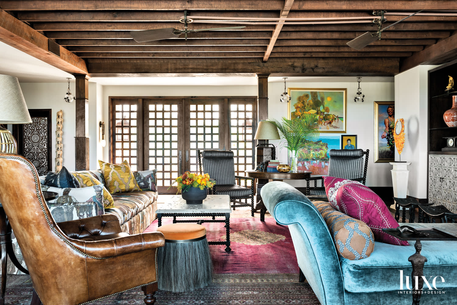 eclectic living area with dark wood ceiling beans, jewel-toned furnishings, fuchsia rug and teal chaise