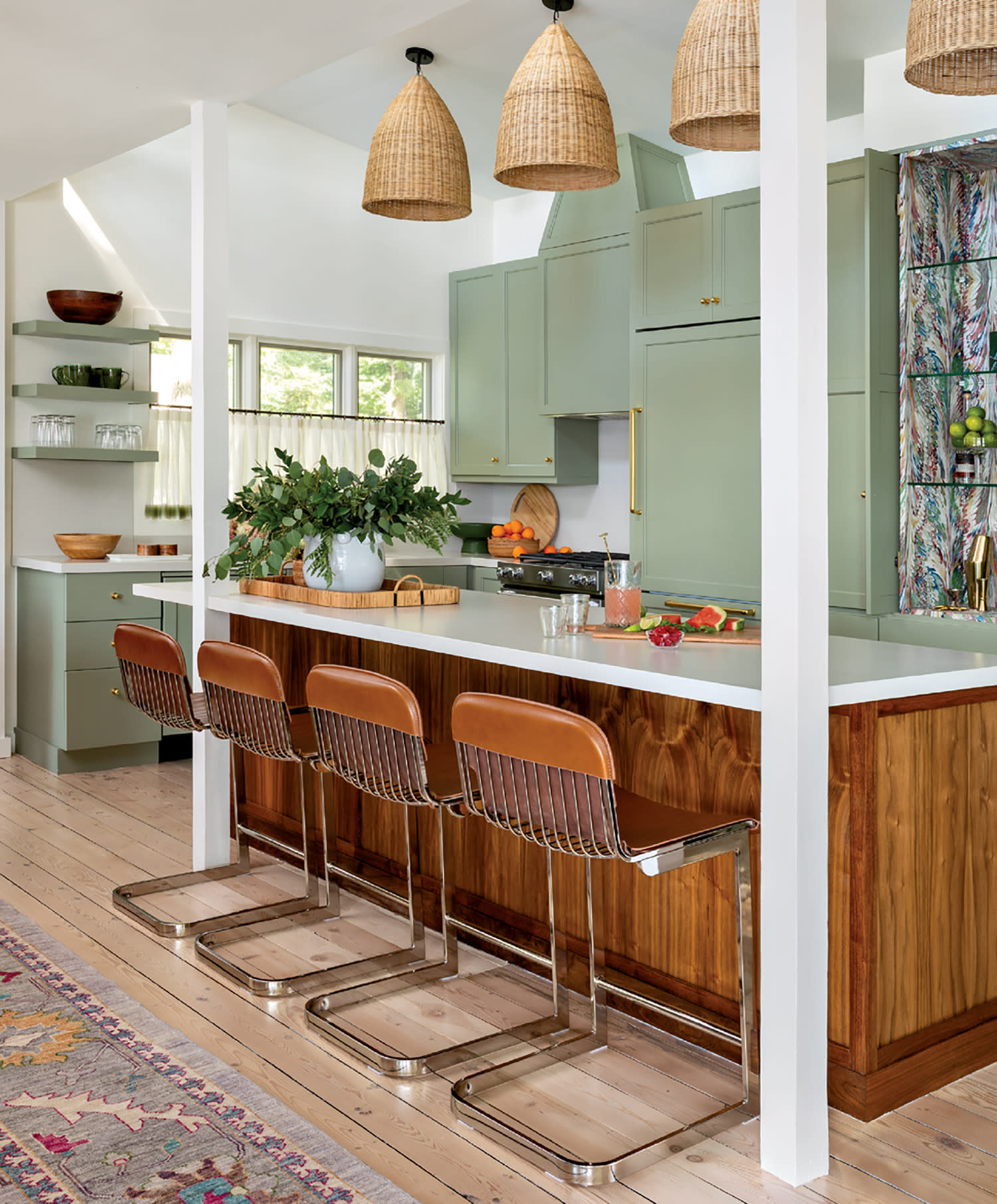 Stylish kitchen with mint green cabinets, wooden island and chairs, wicker pendant lights, and a vibrant rug, creating a warm, inviting atmosphere.