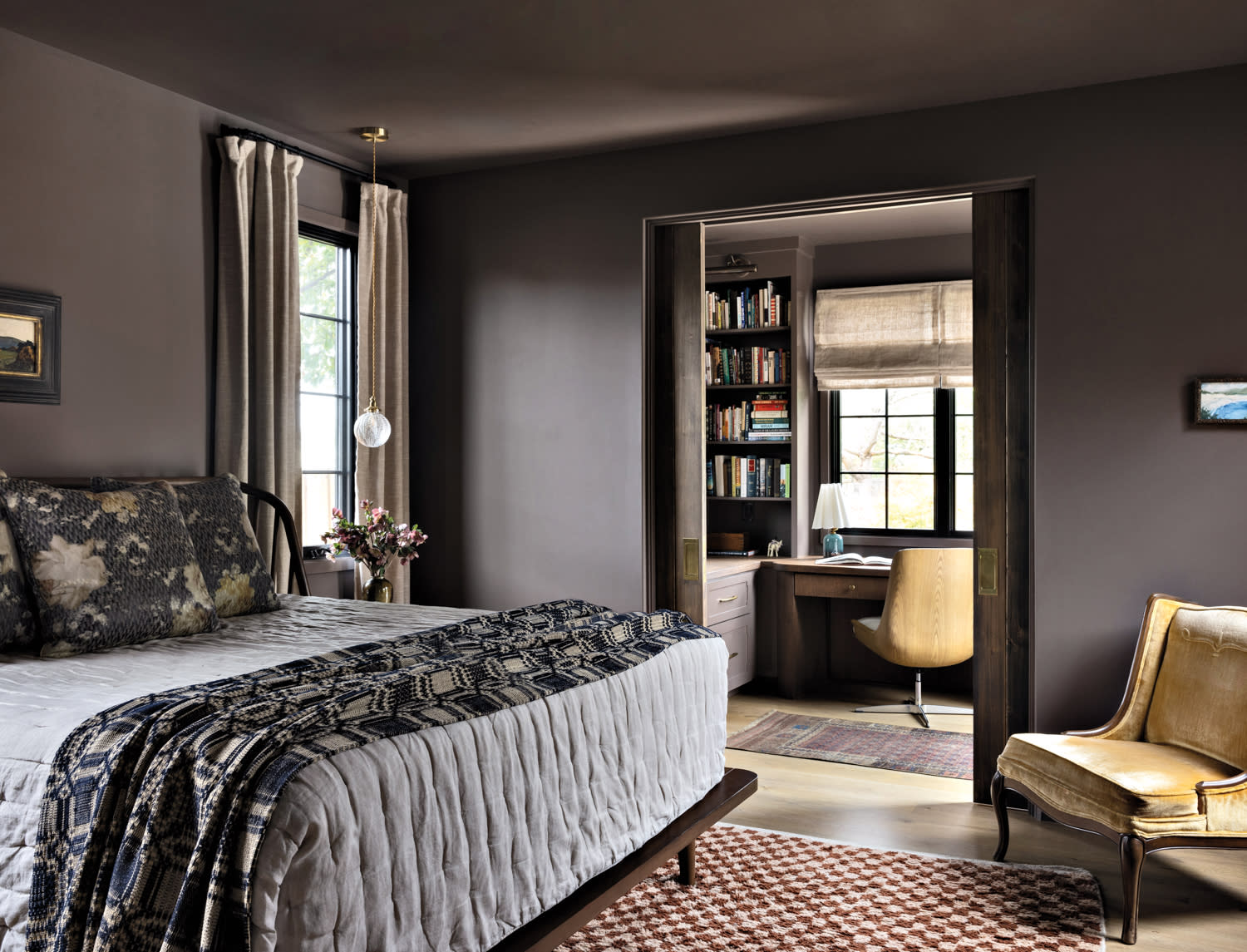 A bedroom with gray walls, linen drapery and a bed with a walnut frame and floral quilt and pillows.