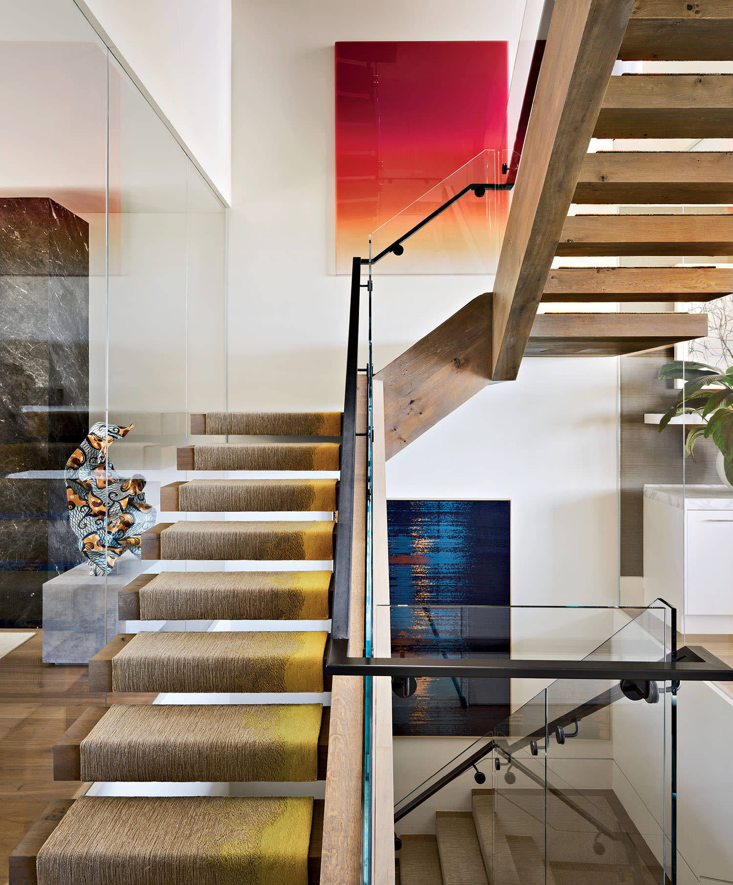 Modern staircase with wooden steps and glass railings in a bright, open space. Abstract art with vibrant colors adorns the walls, creating a sleek and artistic ambiance.
