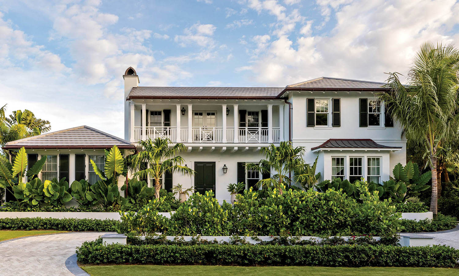 The front exterior of a home painted in white, with a terrace and landscaped greenery out front.