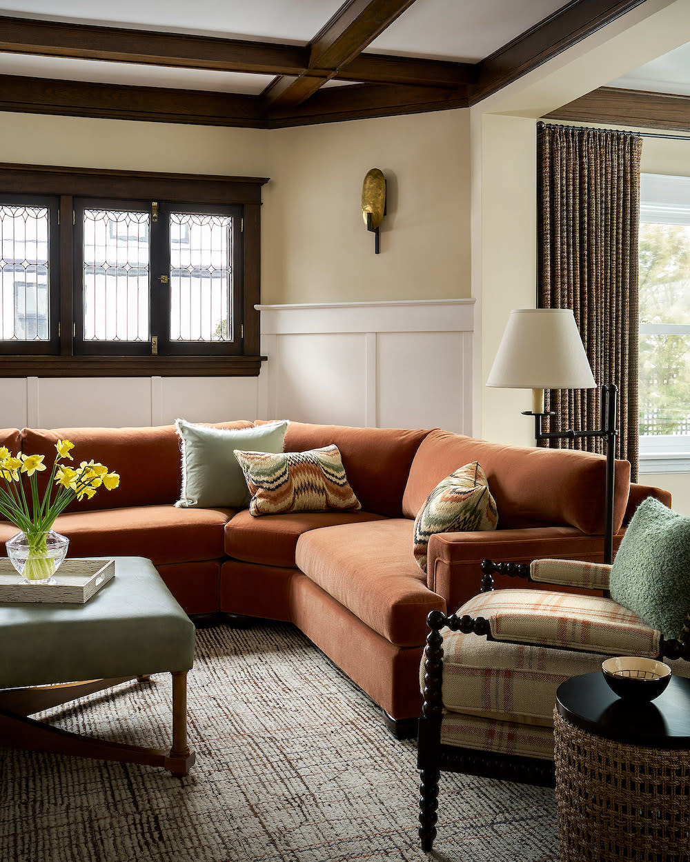 The rust colored velvet sofa in this living rooms warms the dark wood window frame and beams on ceiling.