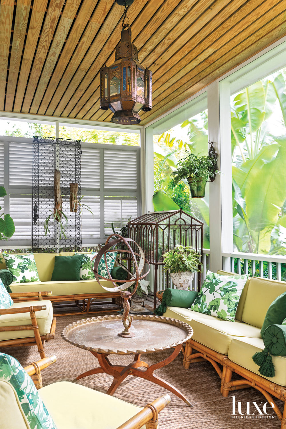 Screened-in porch with yellow sofas, green pillows, a hanging lantern and several live plants