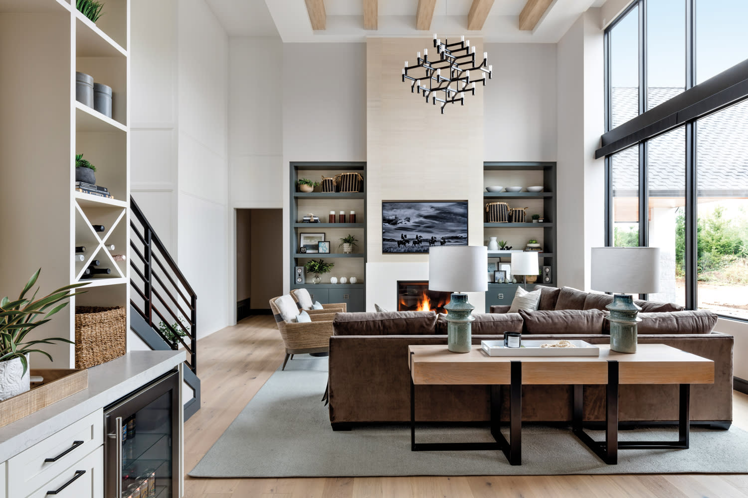 living room with linen colored limestone fireplace, high ceilings with exposed wooden beams, brown sectional and chairs,