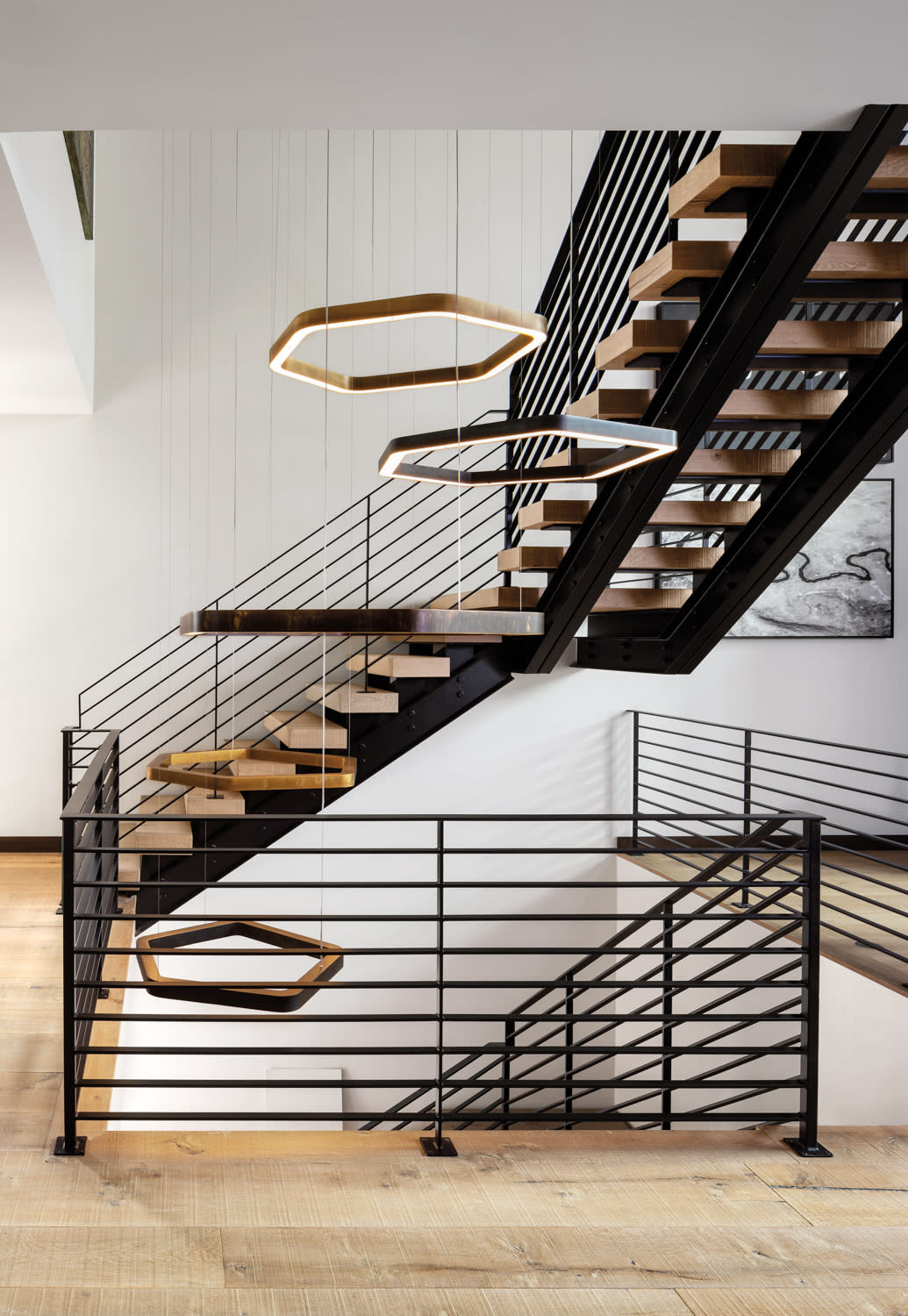 Open steel-and-oak starcase with floating circular lighting fixture hanging in the middle