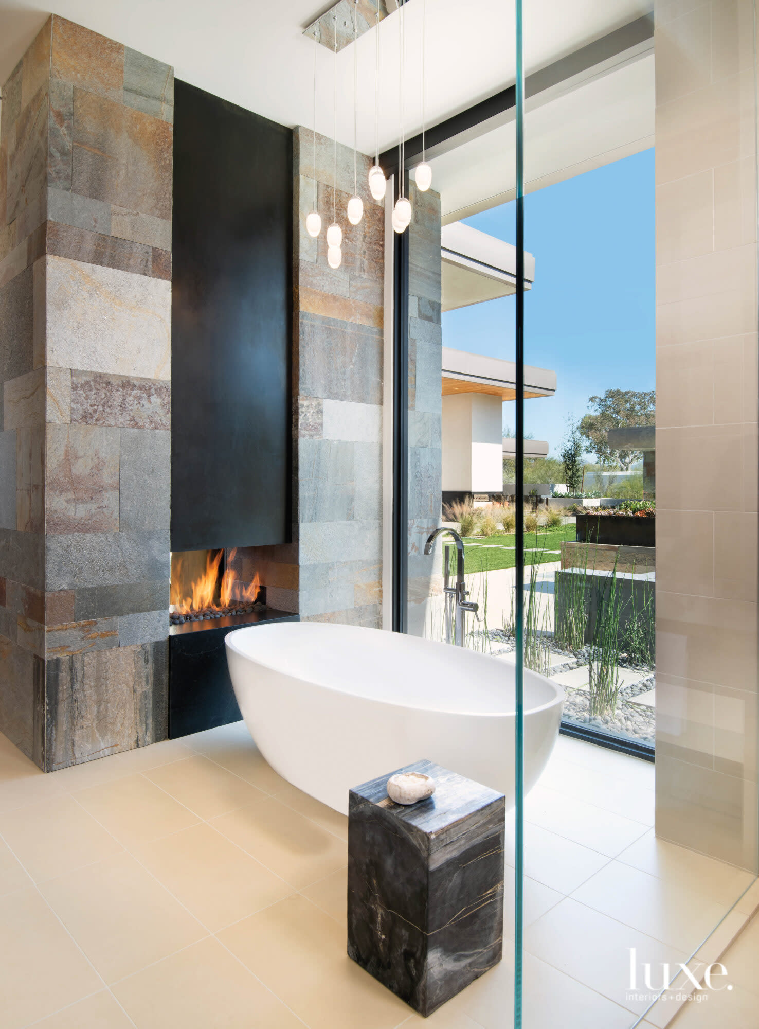 The master bathroom with a freestanding tub, a fireplace and a view outside.