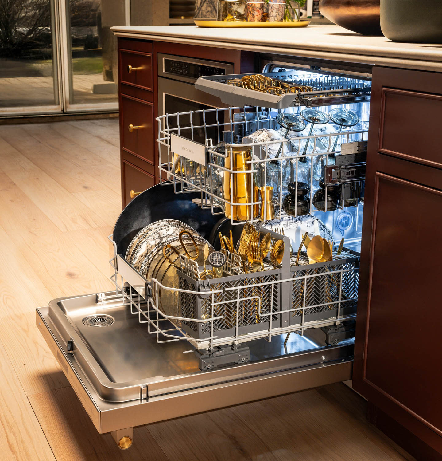 Open dishwasher with a wood finish, filled with shiny dishes, glasses, and gold utensils. Bright lighting creates a clean, organized kitchen feel.