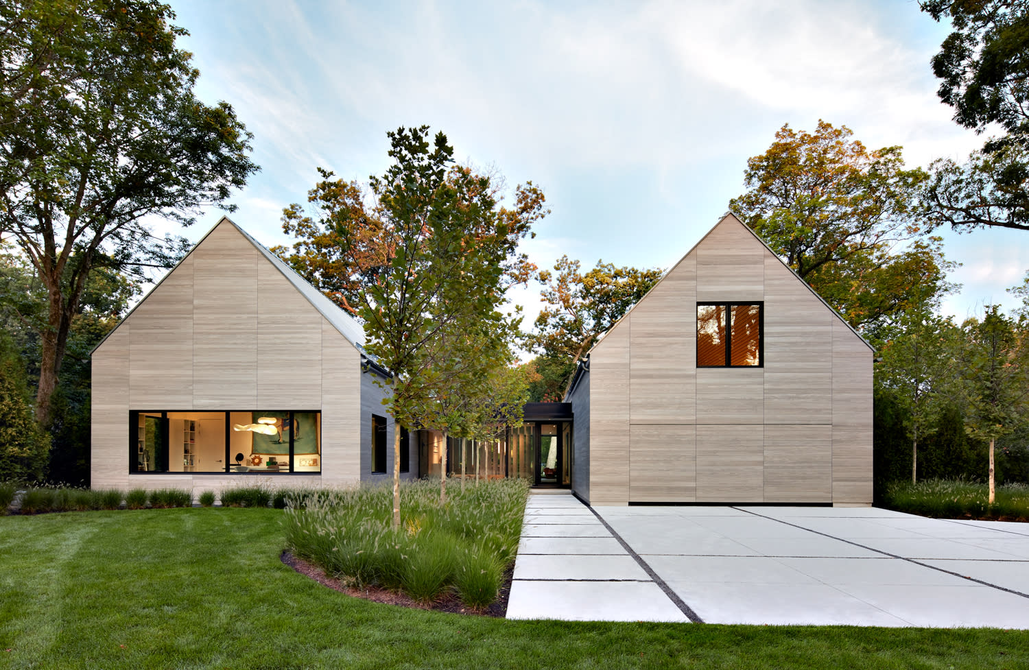 home with light wood exterior and white driveway surrounded by trees