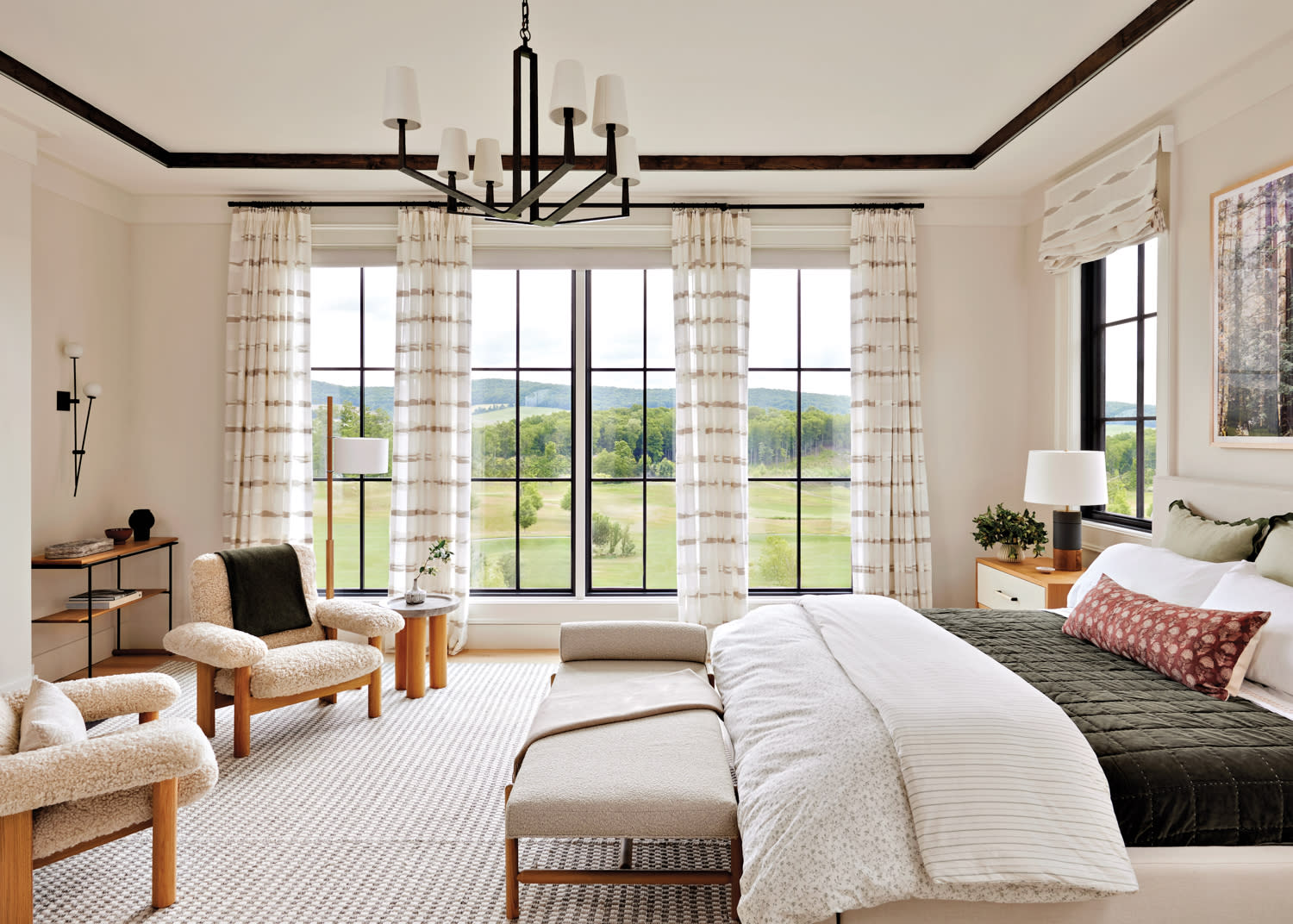 Primary bedroom with shearling chairs, plush bedding, breezy white drapes, chandelier and rug