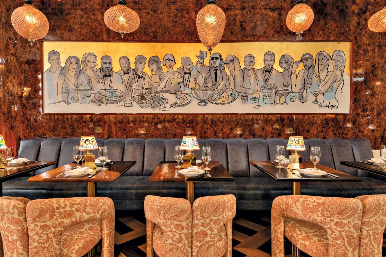 wall art depicting celebrities above a gray-velvet banquette with wooden tables and armchairs