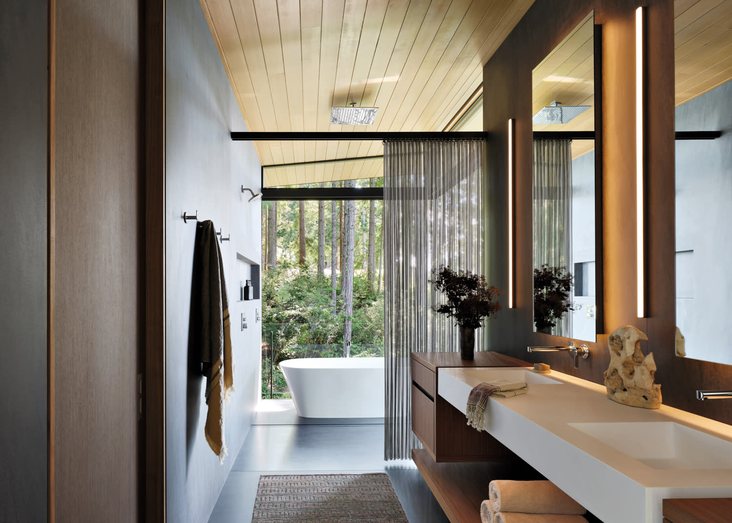 Modern bathroom with a serene vibe, featuring a large window overlooking trees. Highlights include a freestanding tub, sleek vanity, and subtle lighting.