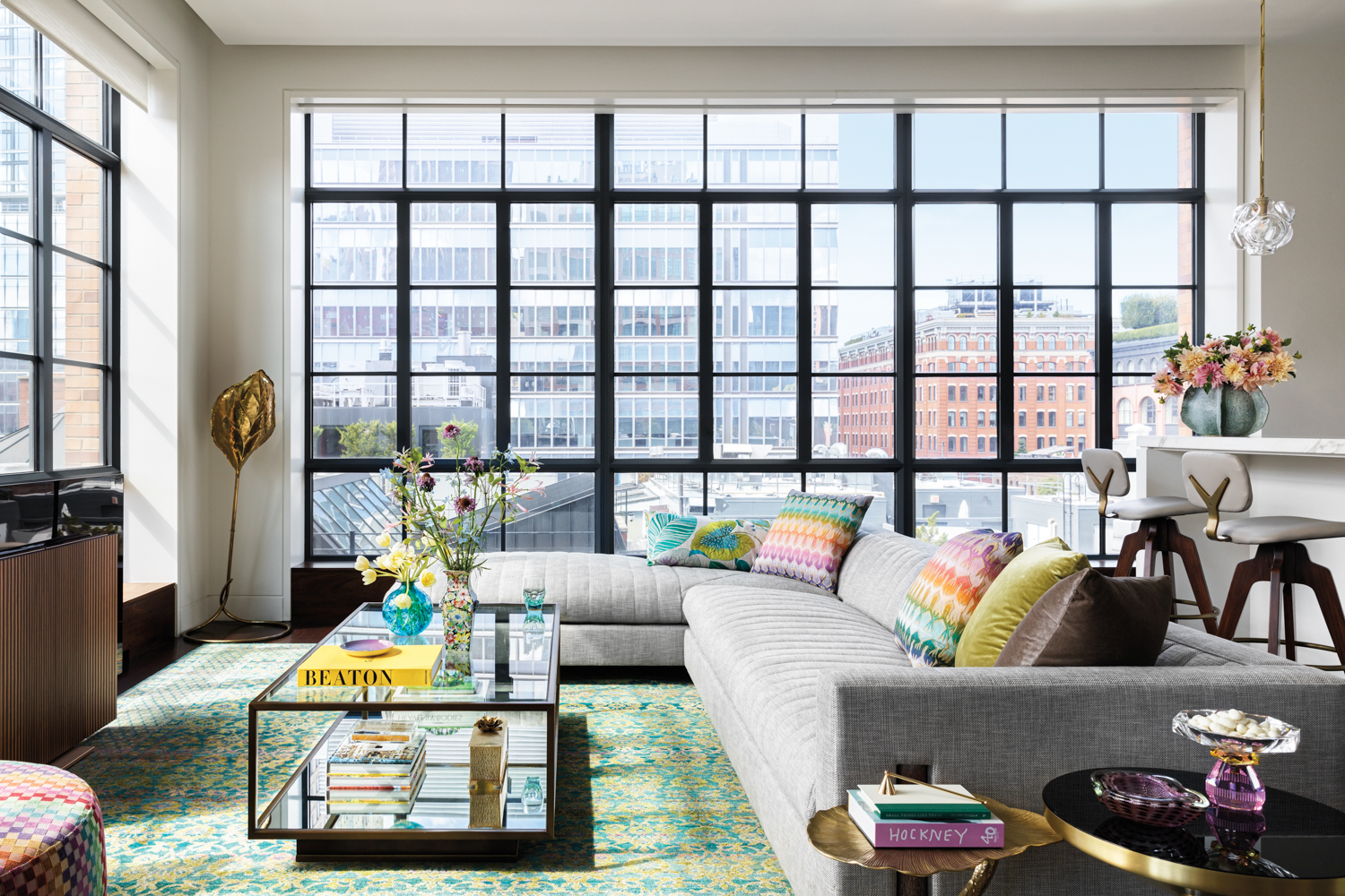 living room with grey sectional and rainbow-colored pillows, glass coffee table and windows overlooking Tribeca