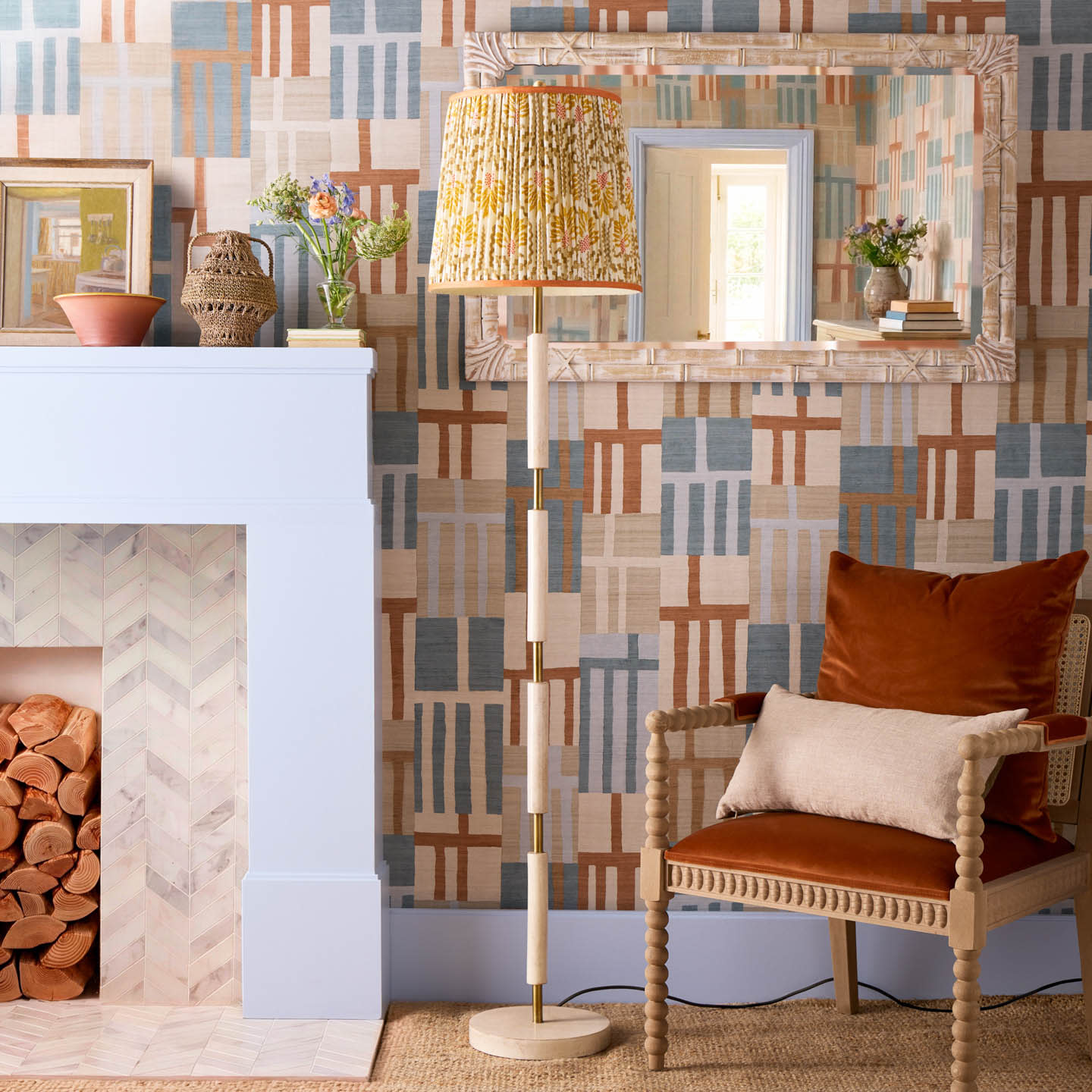 Living room with geometric wallpaper, a cozy chair with rust and beige cushions, a tall patterned floor lamp, and a fireplace with logs. Warm and inviting.