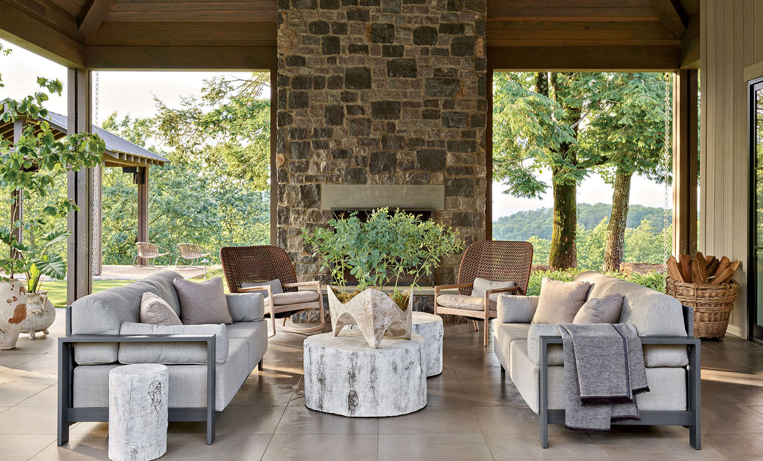A covered outdoor patio area with couches and armchairs, with two coffee tables and a fireplace.