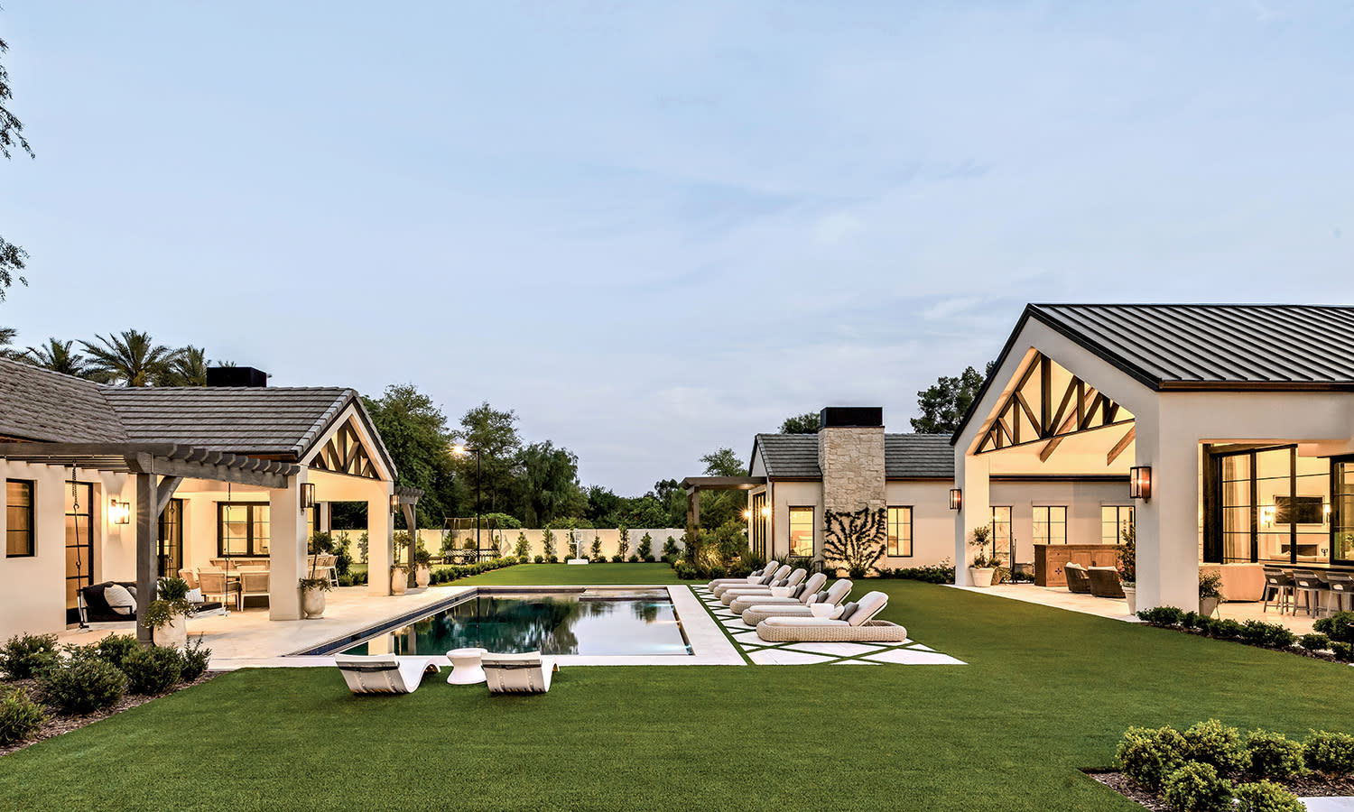 Luxurious villa with two modern buildings, a central pool, and manicured lawn. The setting conveys elegance and relaxation under a clear sky.