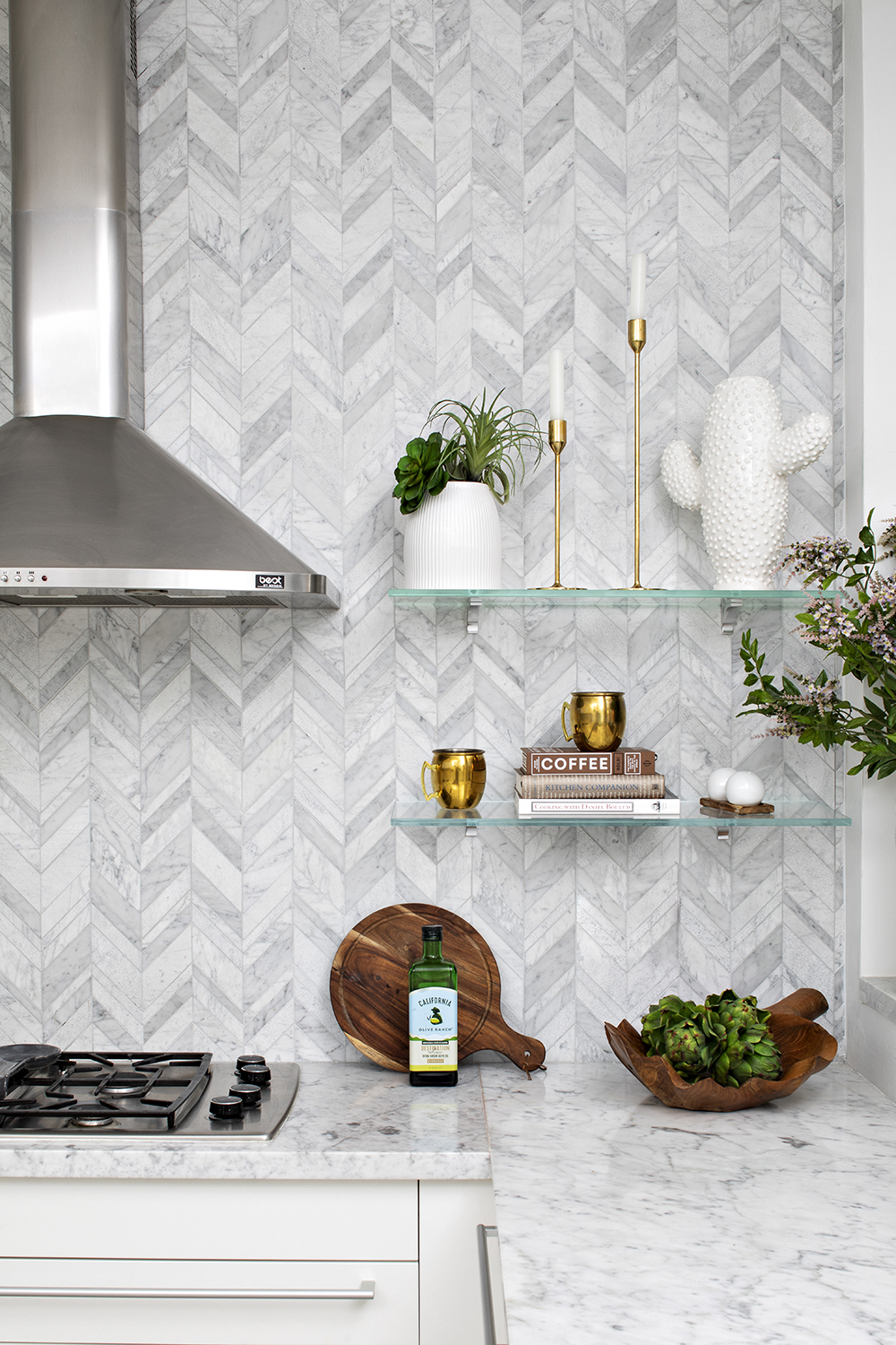 kitchen vignette with gray marble tile backsplash tile in chevron pattern, marble countertops and silver range hood