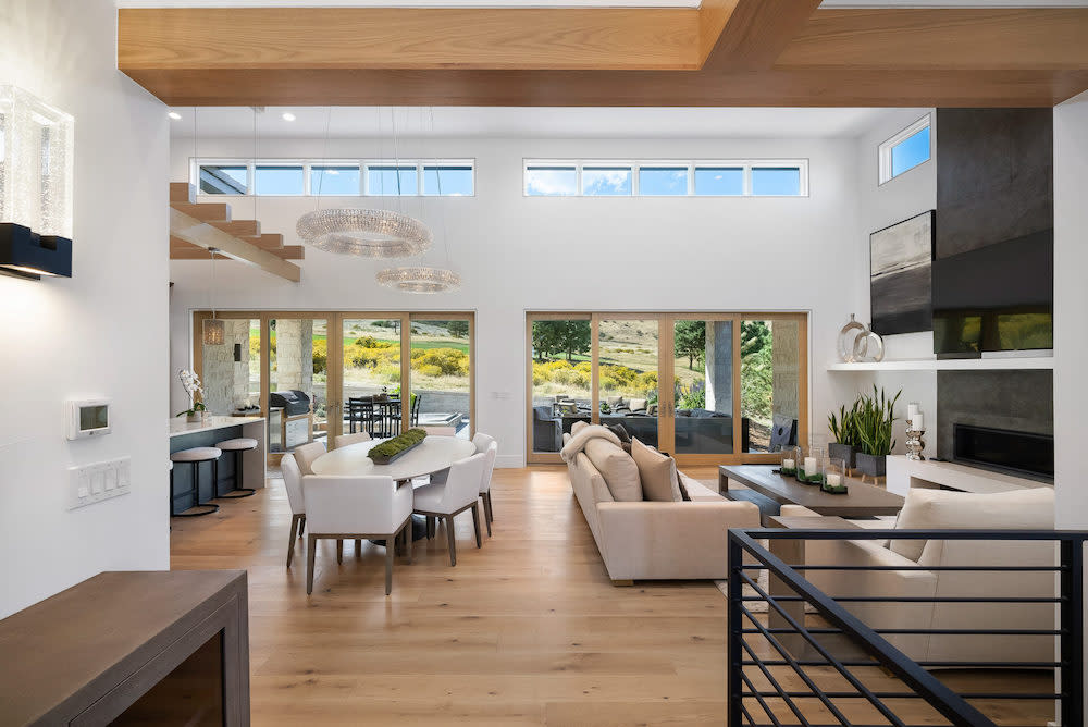 Large, open living space with wall of windows. White walls, light wood wide plank floors and exposed light wood beams complete the space.