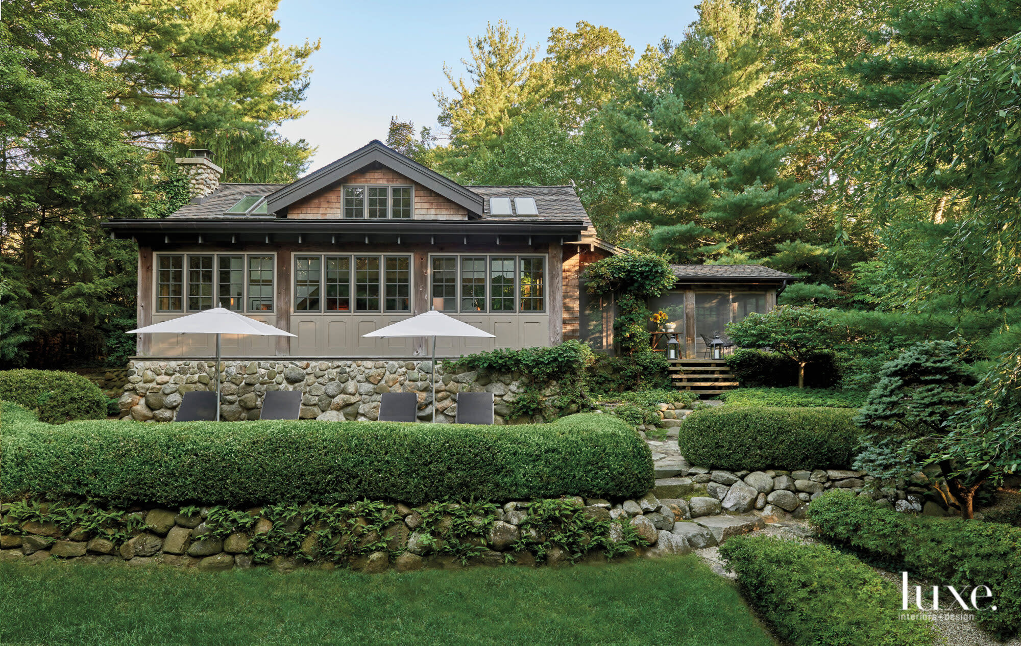 Lounge chairs sit in front of a stone wall outside of the cabin, surrounded by greenery.