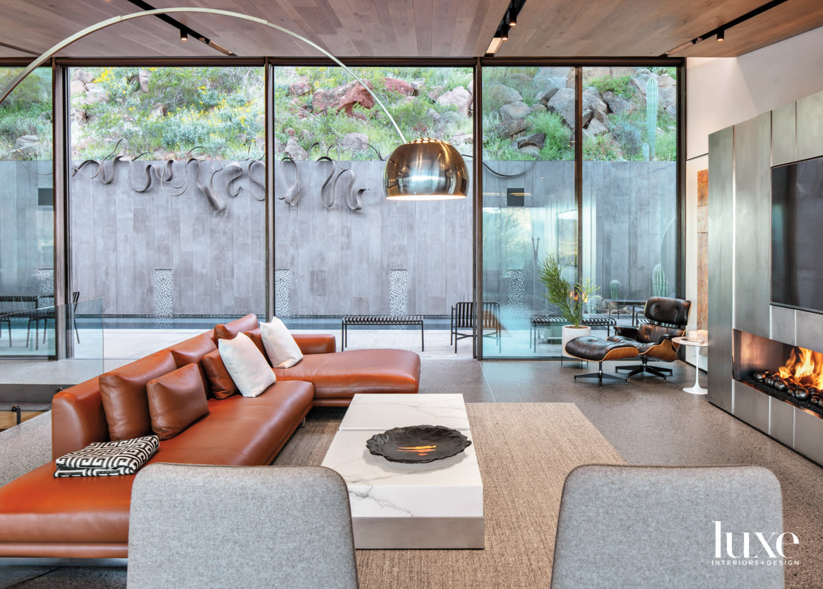 A living rooom with a low-profile leather sectional and marble-and-metal coffee table. In the corner is an Eames lounge chair and ottoman.