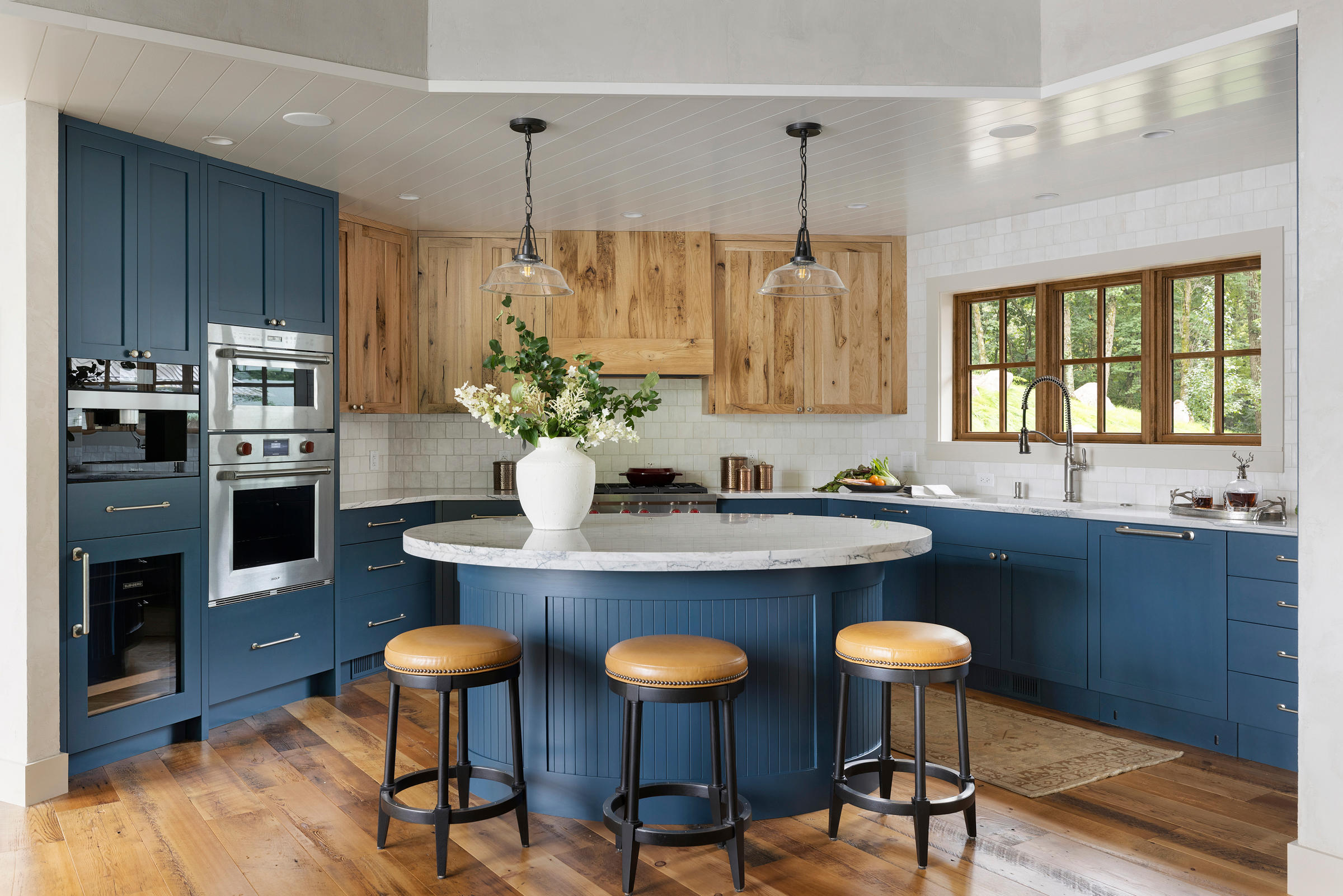 This custom build home features a beautiful kitchen complete with a circular island with a double-thick marble counter, bold blue cabinetry, and rustic wood finishes. 
Photography by Spacecrafting