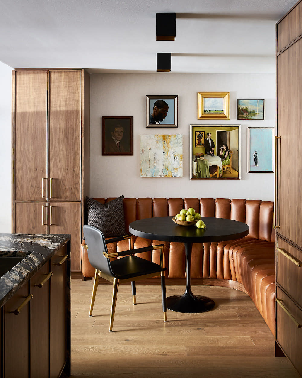 The nook of this kitchen includes a leather banquette with black circular table and gallery wall.