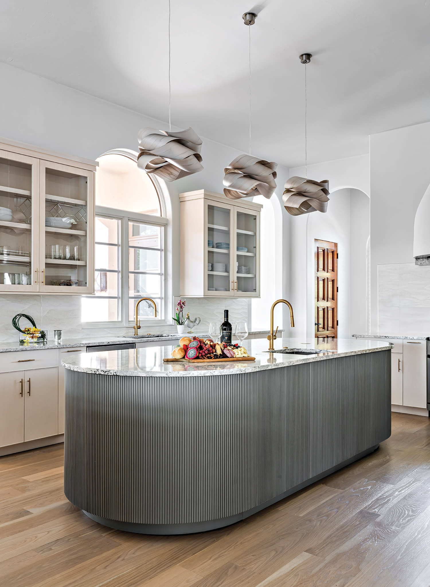 Modern kitchen with a light wood floor, curved gray island, and marble countertop