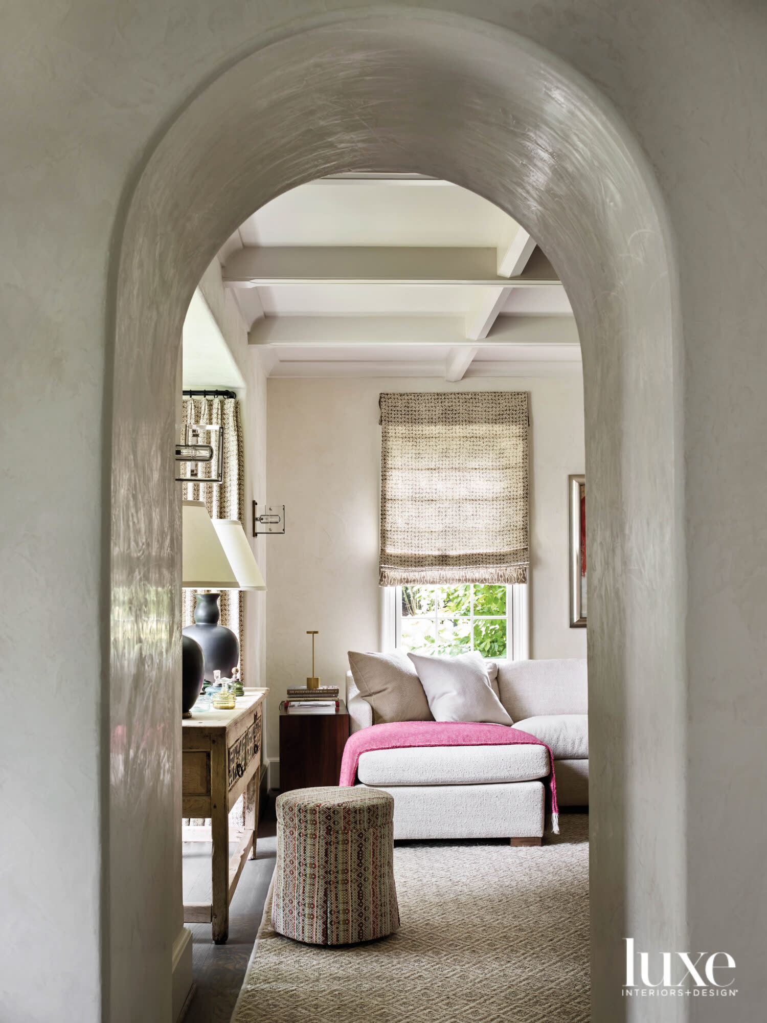 Arched doorway peering into a living room with an L-shaped sofa and bright pink throw