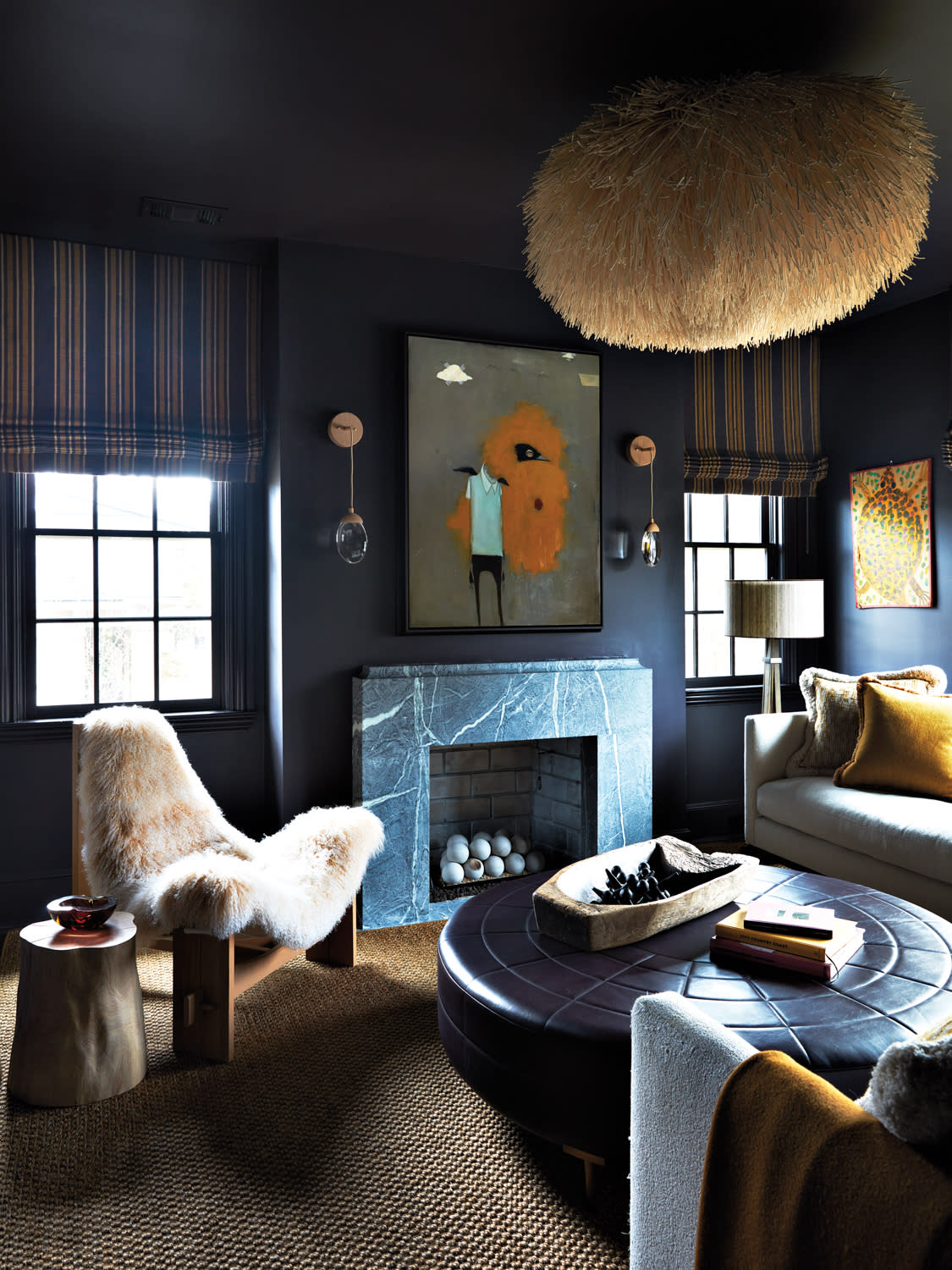 Dark den featuring a furry lounge chair, folk-inspired artwork, leather ottoman and dramatic light fixture