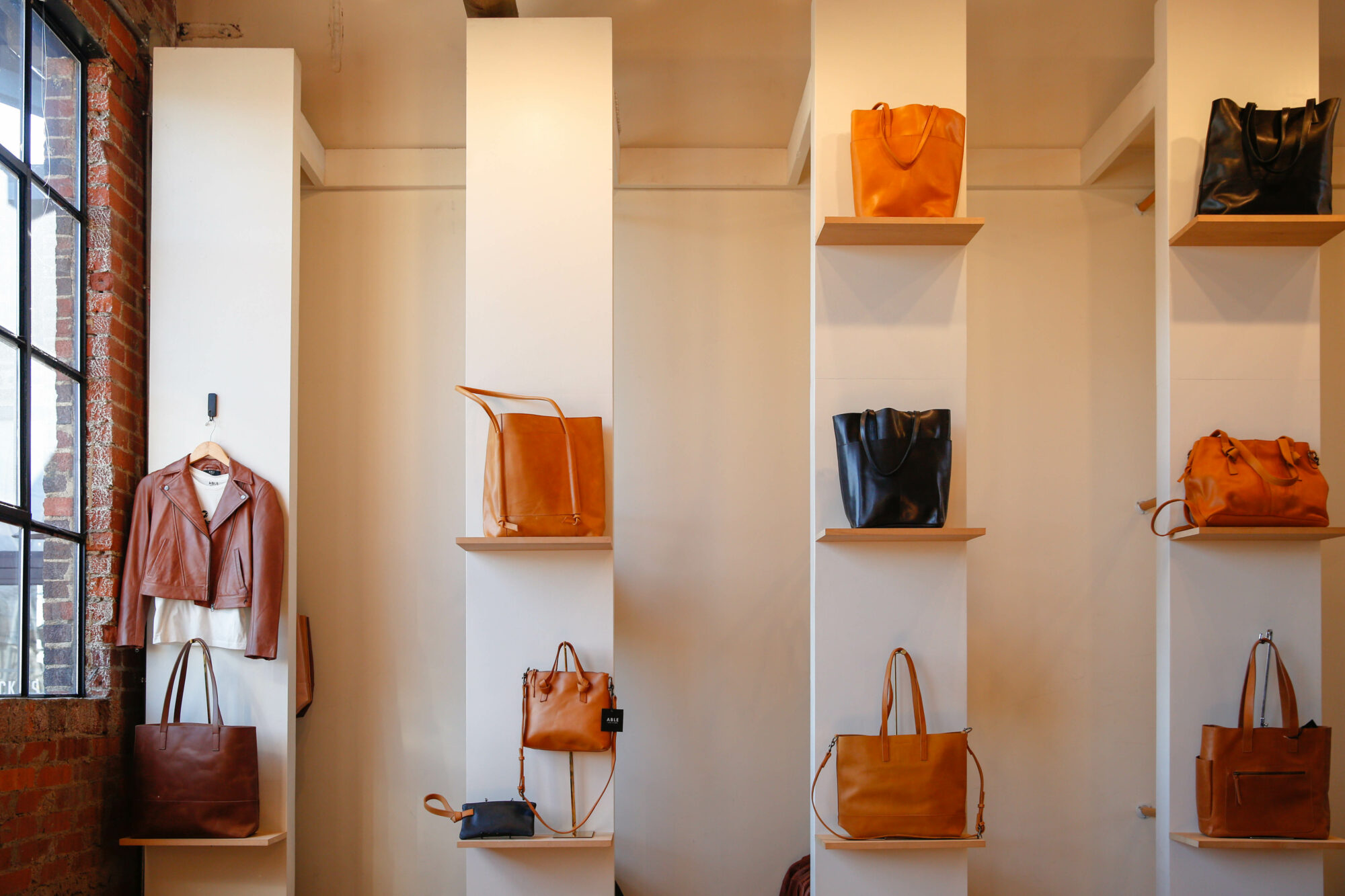 Black and tan leather handbags on their own wooden shelves lining white columns