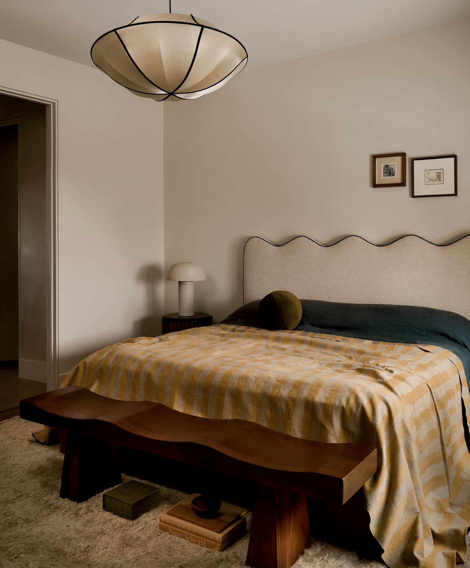 A cozy bedroom featuring a wavy beige headboard, checkered yellow blanket and wooden bench