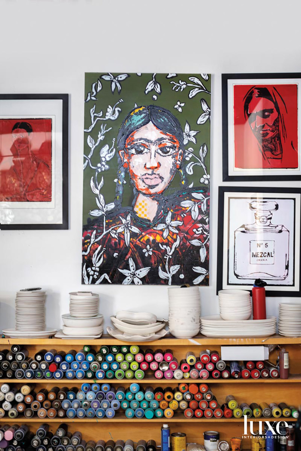 A group of paintings above shelves with ceramics and paint