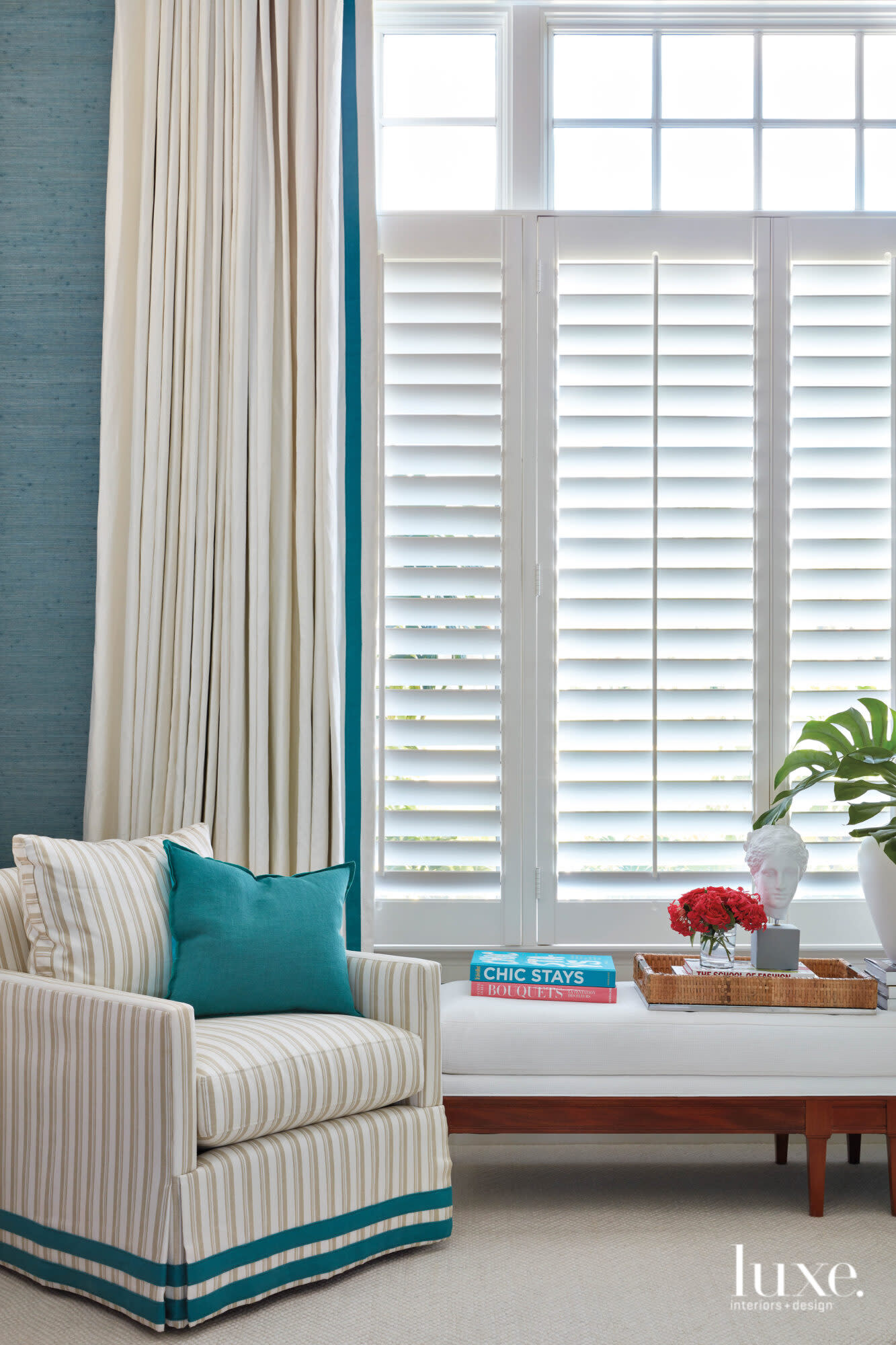 Bedroom with stripped armchair and white bench against an aqua wallcovering.