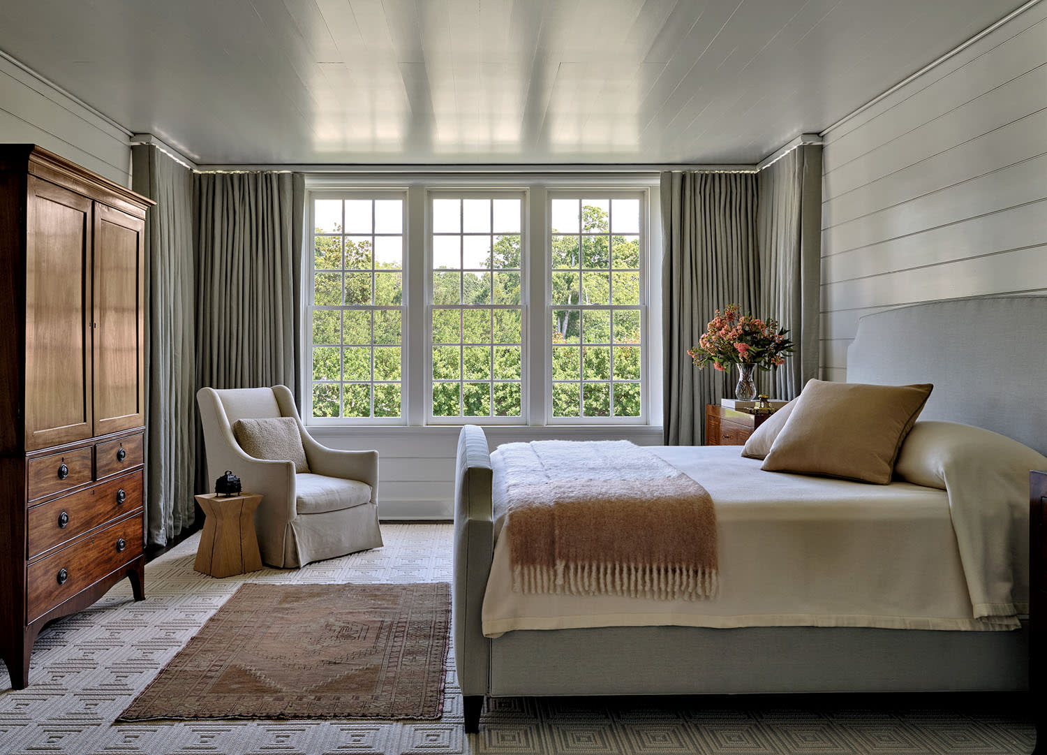 A cozy bedroom featuring a bed, dresser, chair, and a window allowing natural light.
