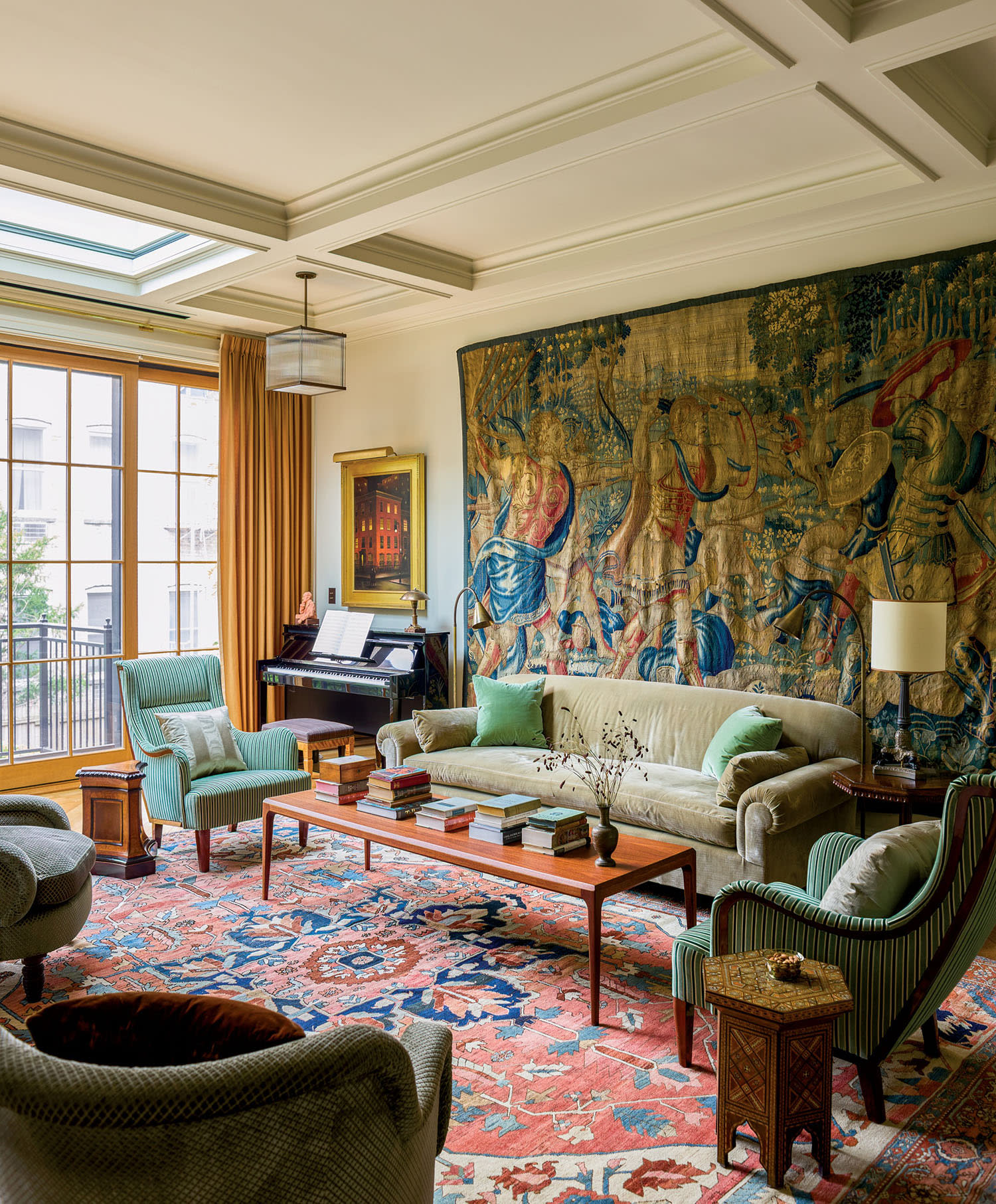 Elegant living room with antique tapestry, plush sofas, armchairs, a grand piano, and vibrant red-patterned rug. Bright natural light filters through large windows.