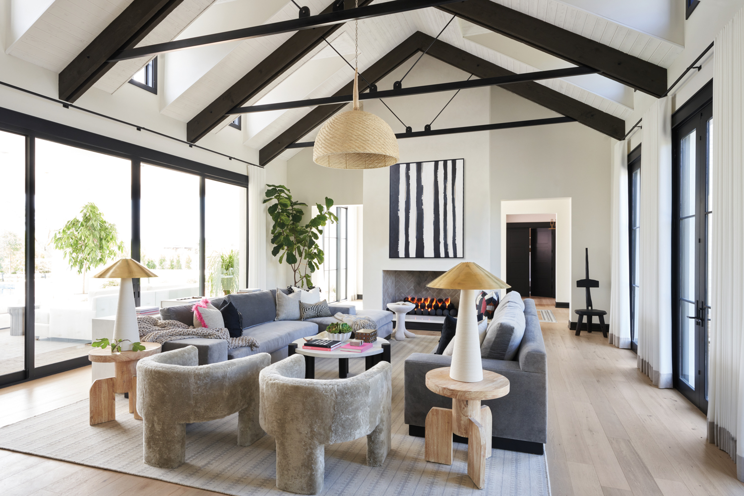 A seating are with two gray couches and two curvy armchairs surrounds a fireplace, above which hangs a black-and-white abstract artwork.