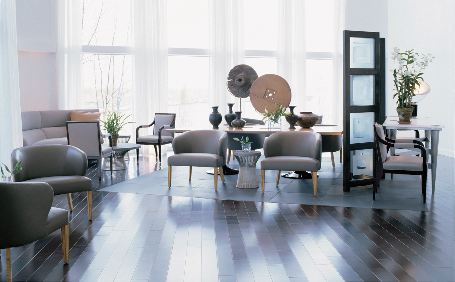 Interior with four floor-to-ceiling windows, grey chairs as well as vases and wheel-shaped artwork on a table