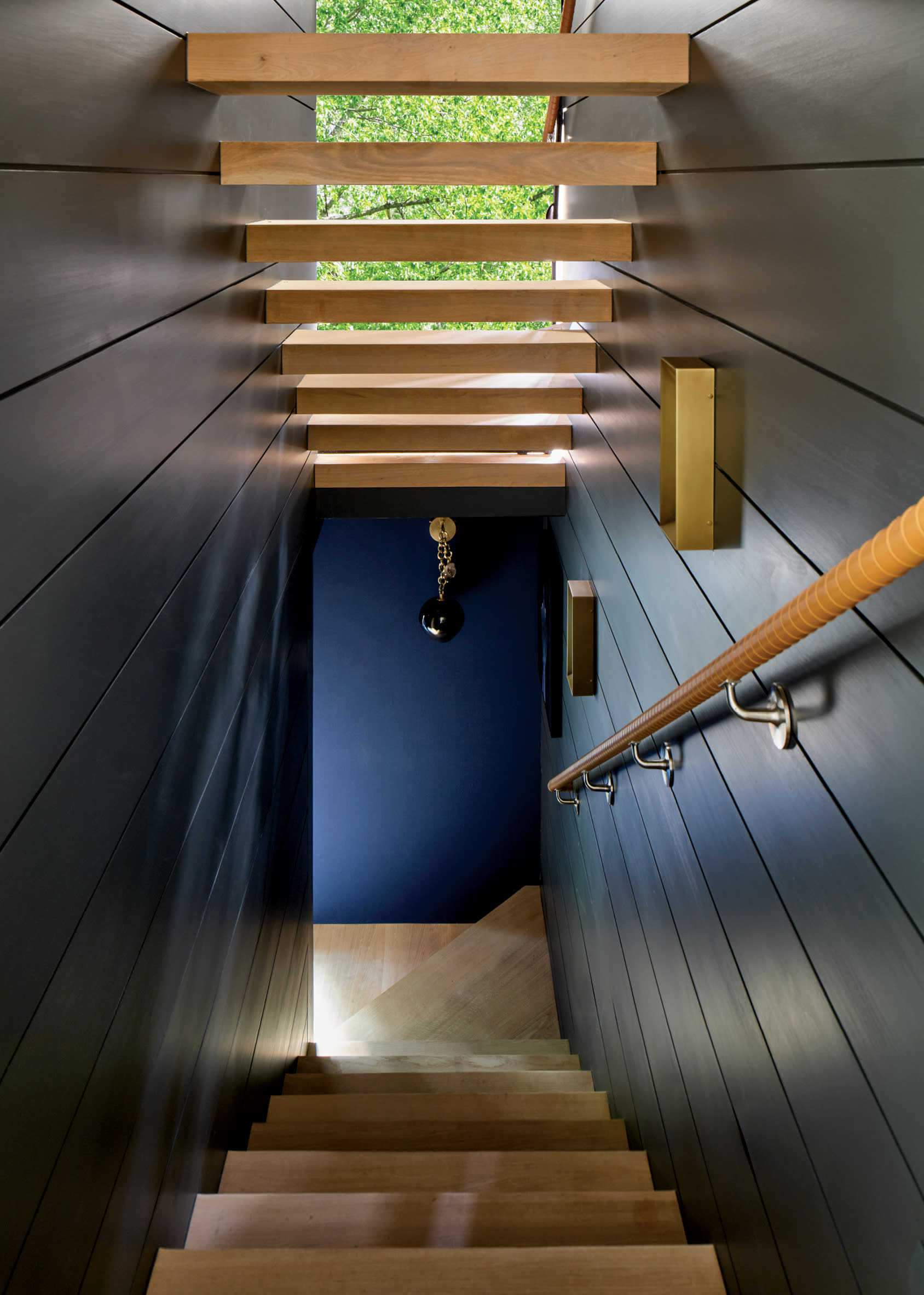 stairwell lined with dark walls with daylight floating in from oak treads above