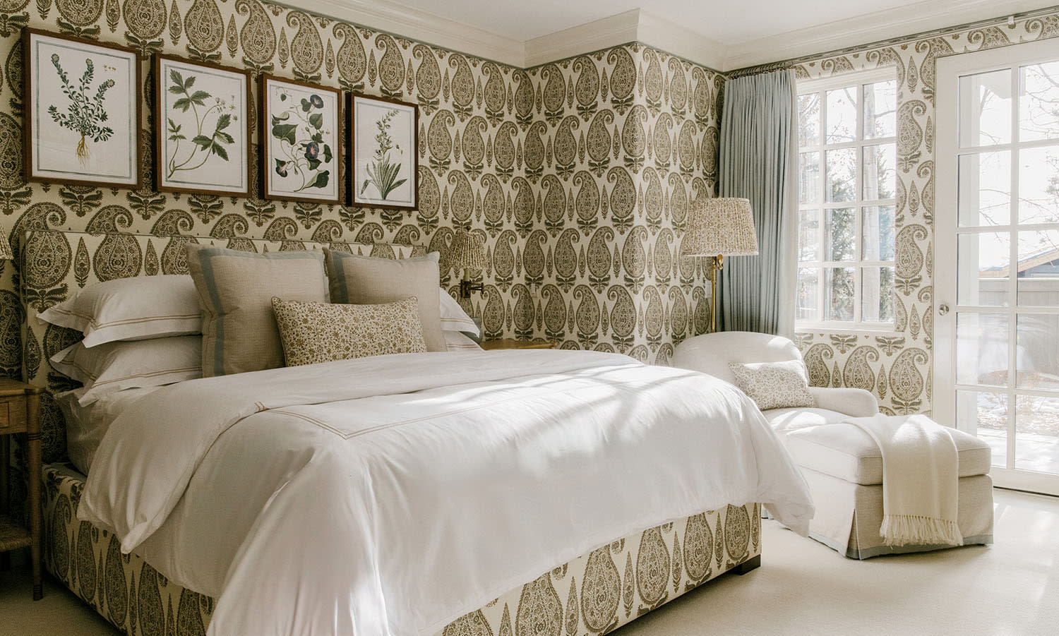 Green and white patterned wallpaper in a bedroom with a matching headboard and framed photos of plants.