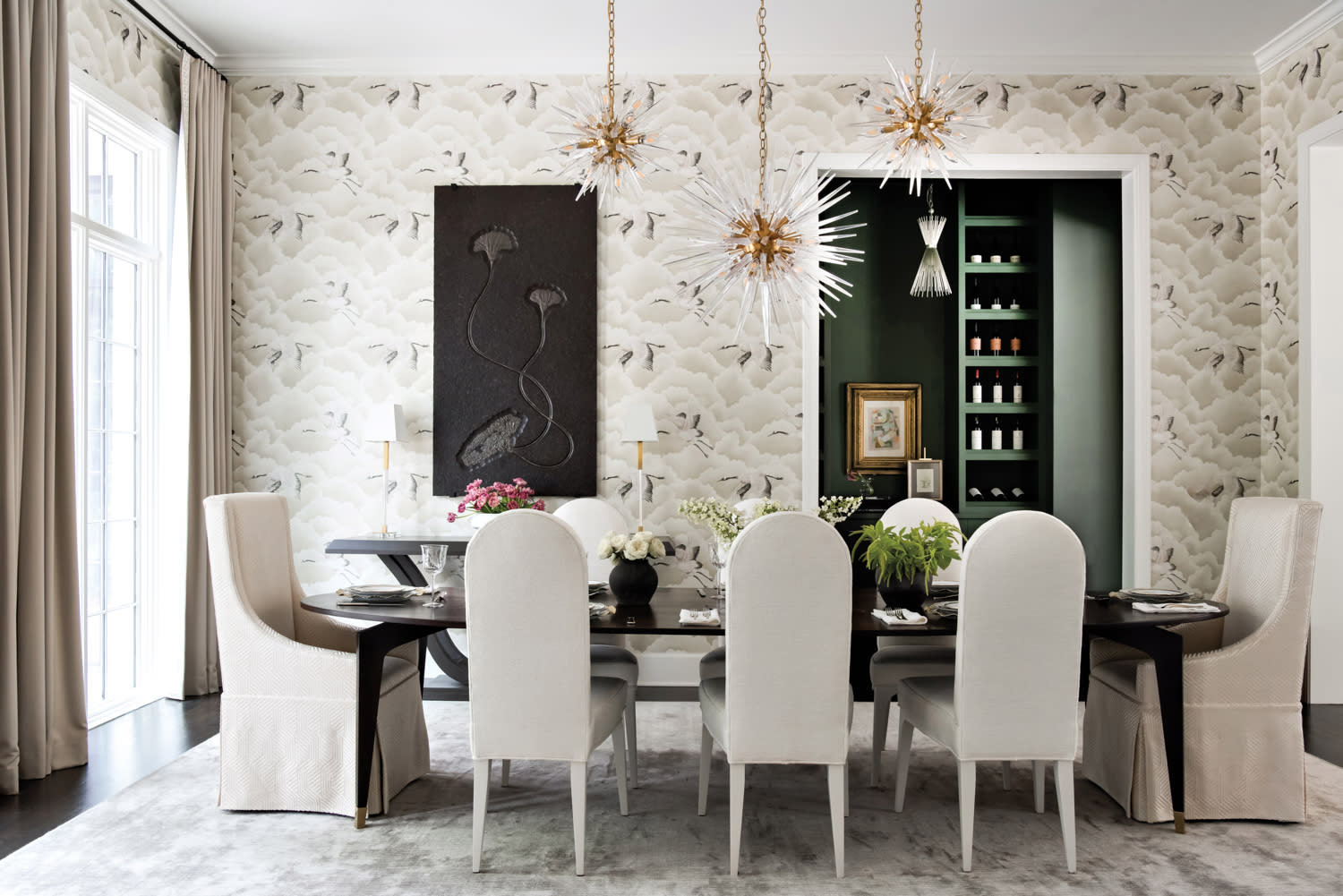 Bold dining room with curved-back chairs, Sputnik-style chandeliers and avian-print wallpaper